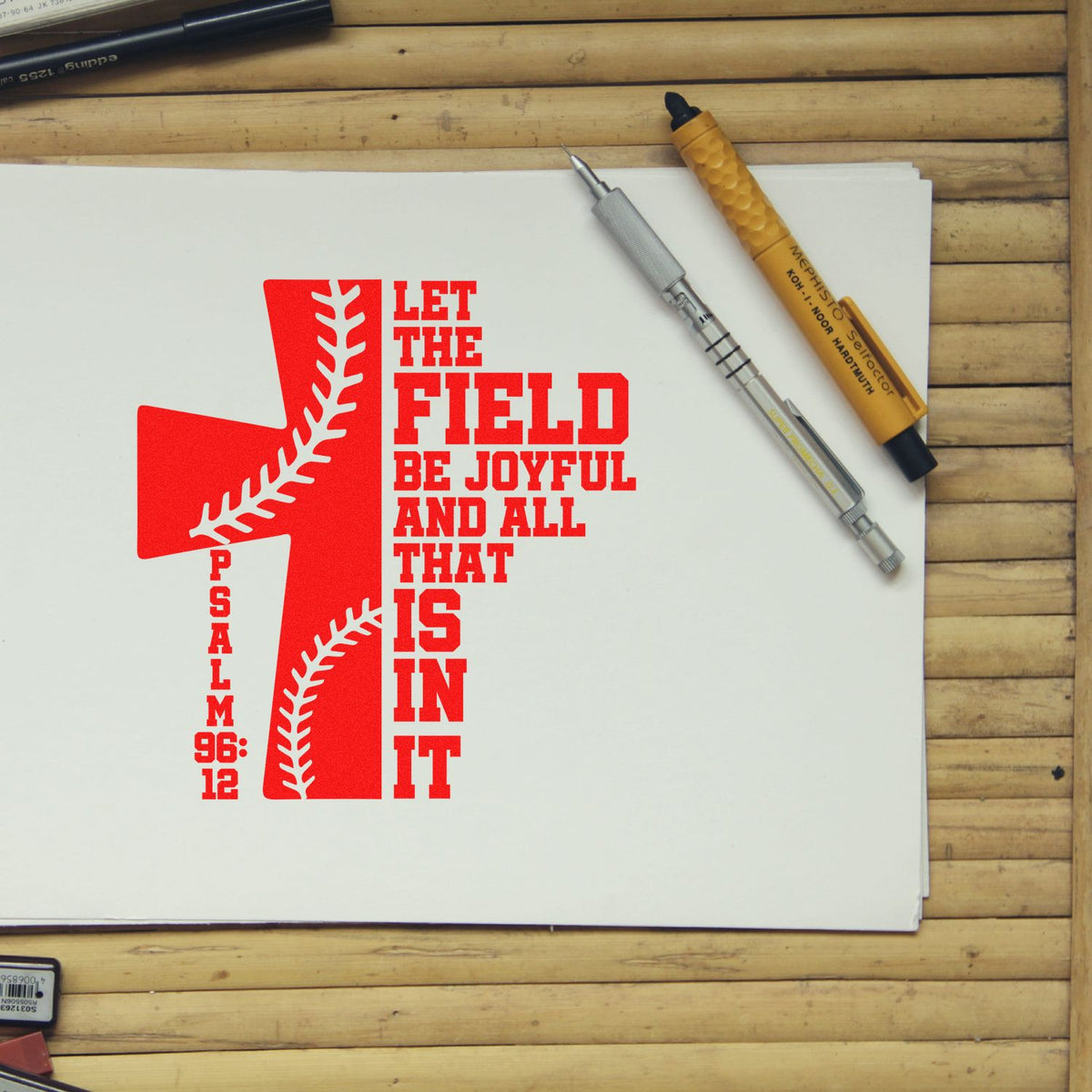 Red baseball-themed stamp on white paper with Psalm 96:12 text, beside silver and orange stamp-and-seal tools on a wood desk.