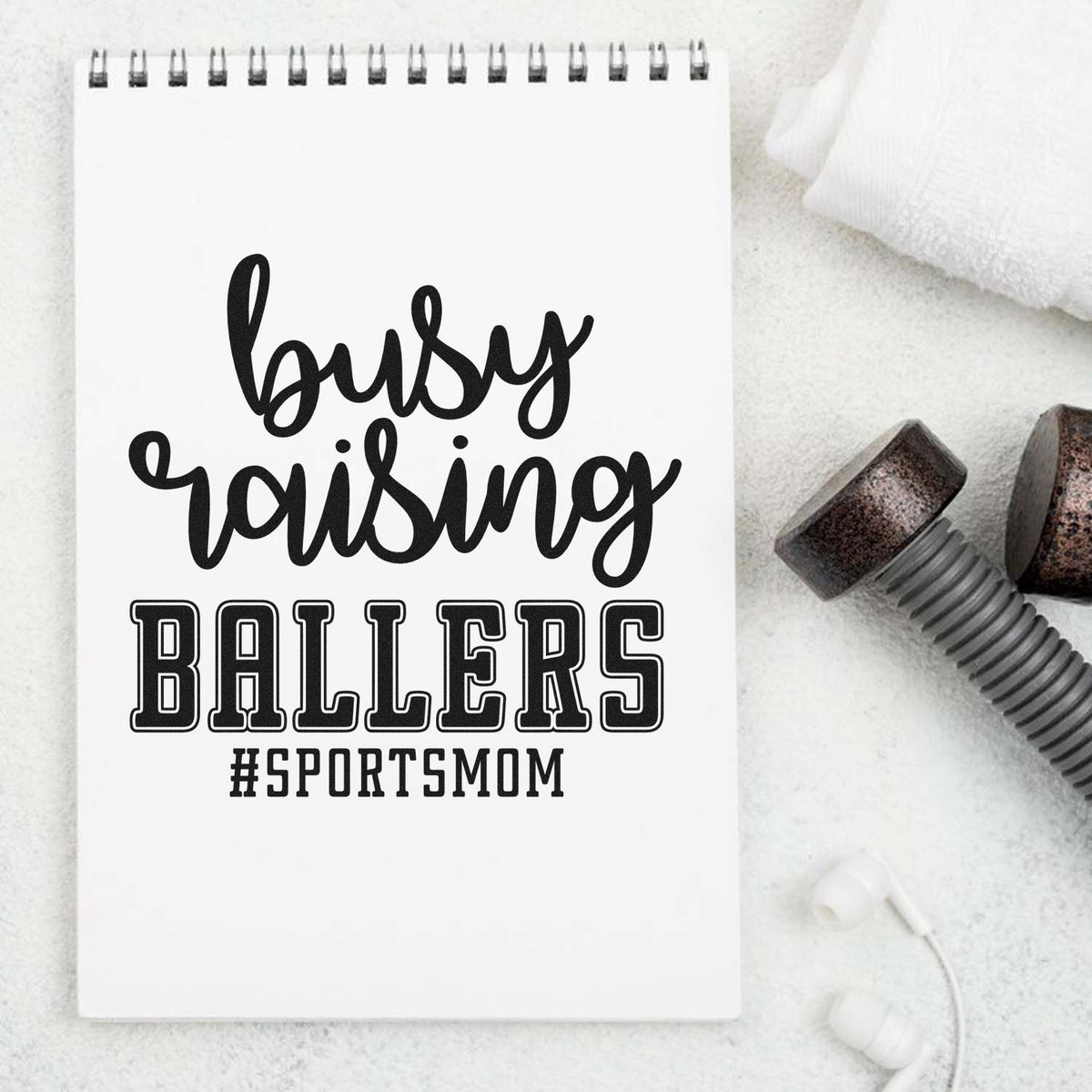 White spiral notebook with black busy raising BALLERS #SPORTSMOM design beside black stamp and seal products on a white background.