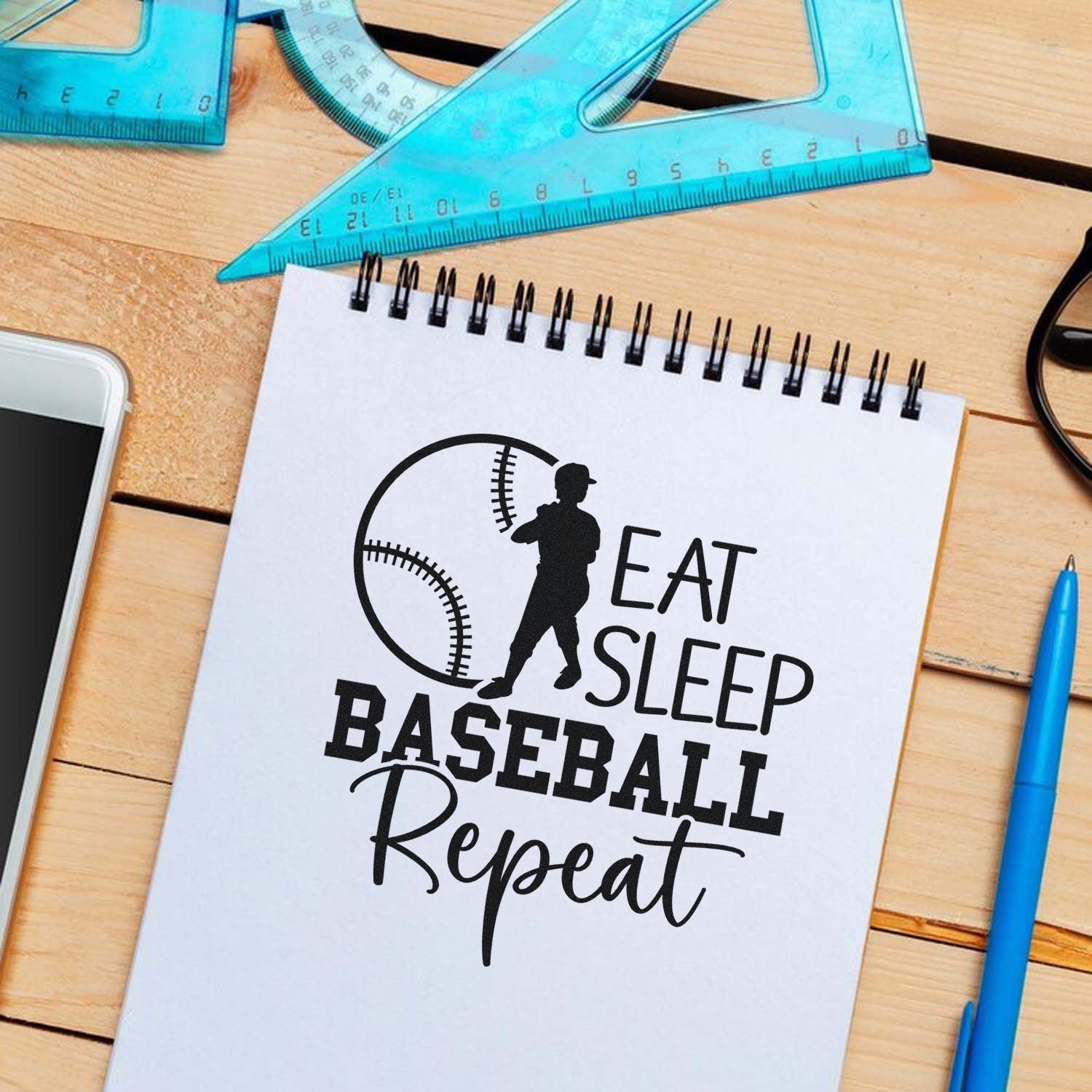 Black baseball stamp and seal design on white notebook, with Eat Sleep Baseball Repeat text and blue rulers.