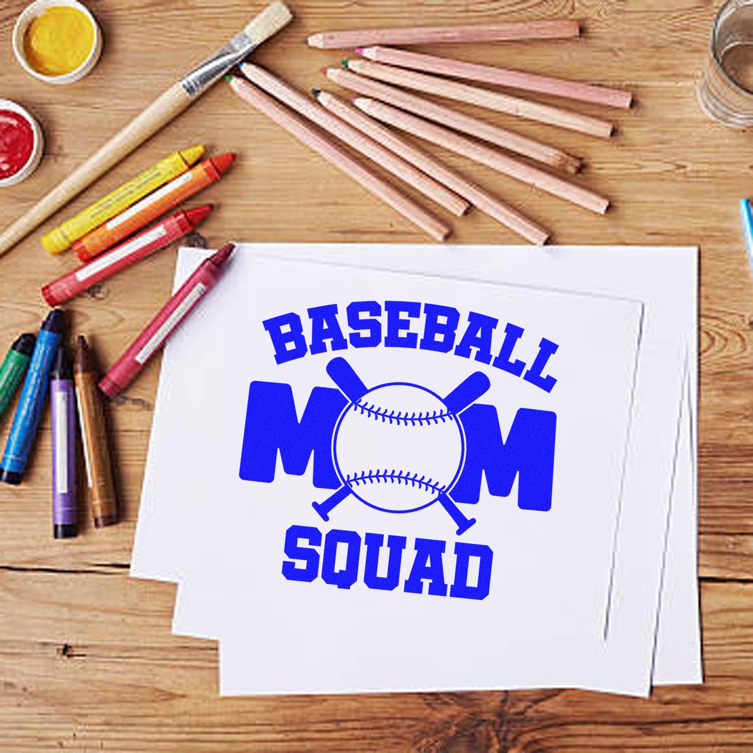 Blue Baseball Mom Squad stamp design on white paper, with pencils, crayons, and seal-making supplies on a wooden table.