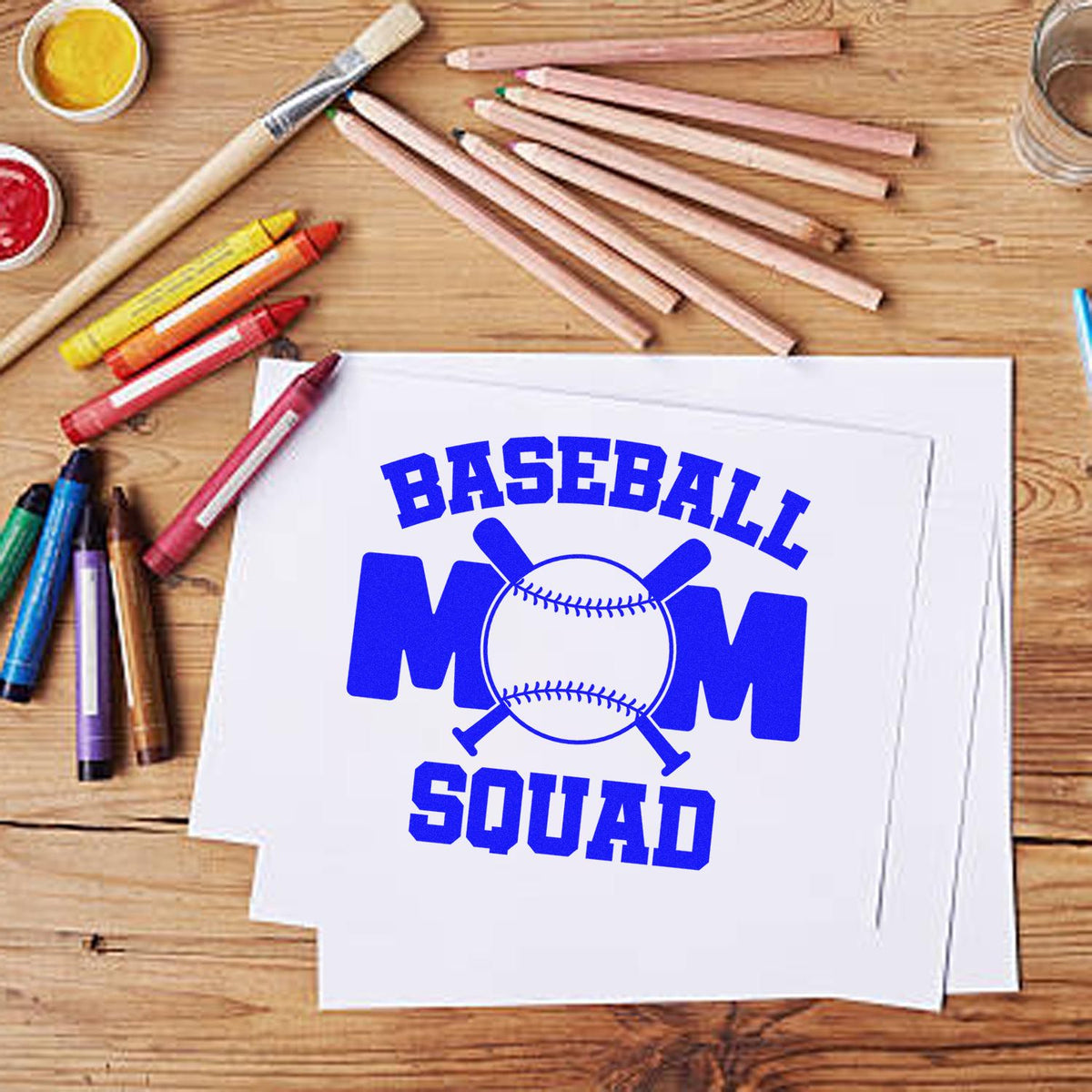 Blue baseball mom squad stamp and seal design on white paper, with bat-and-ball graphic and colored pencils.