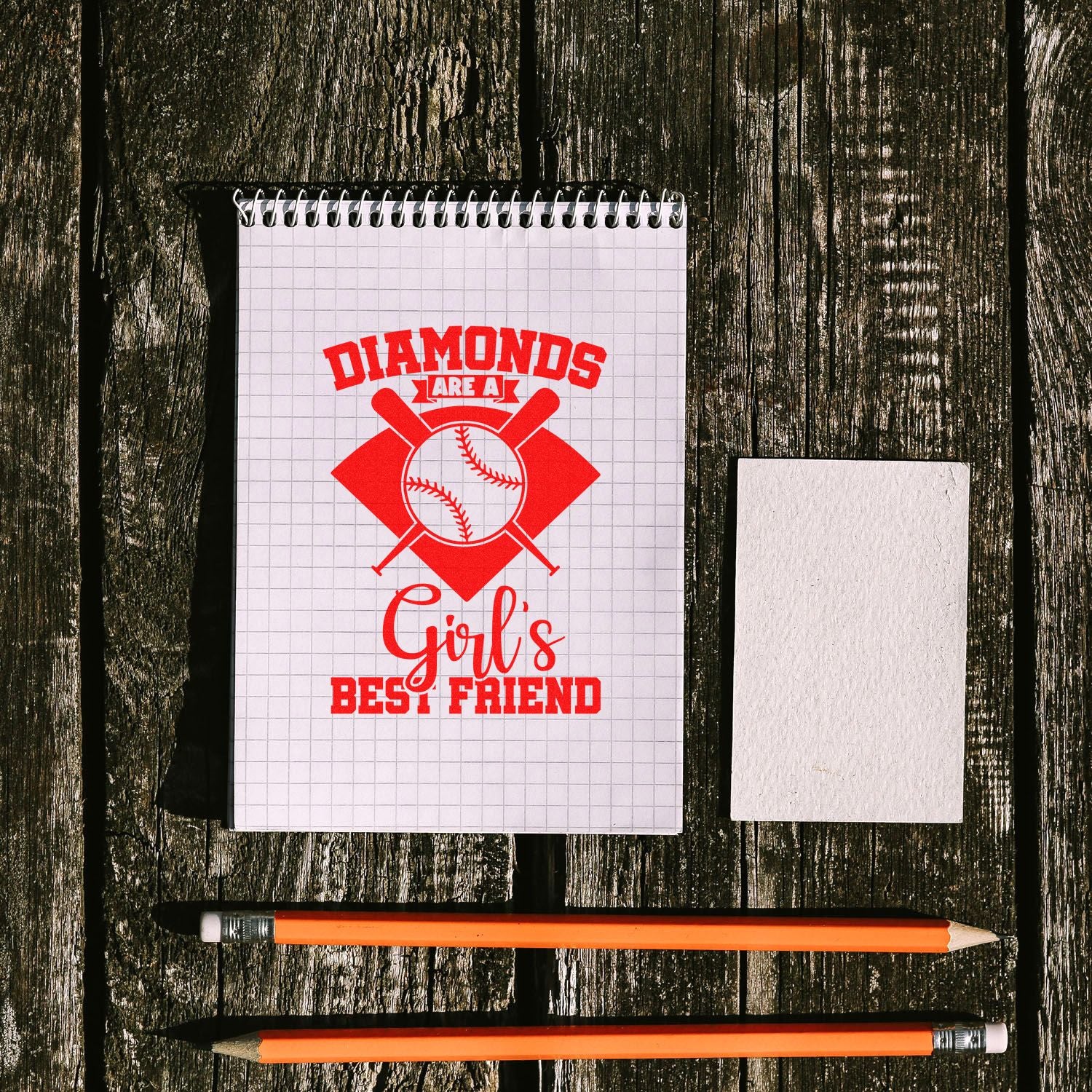 Red baseball stamp and seal design on a grid notebook reading Diamonds are a Girls Best Friend, with eraser and orange pencils.