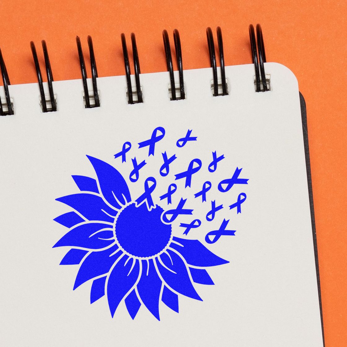 Blue sunflower and awareness ribbons stamp and seal on white spiral notebook with orange background.