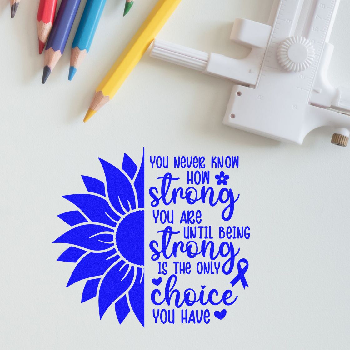 Blue stamp and seal with sunflower and motivational quote, shown beside colored pencils and a white stamping tool