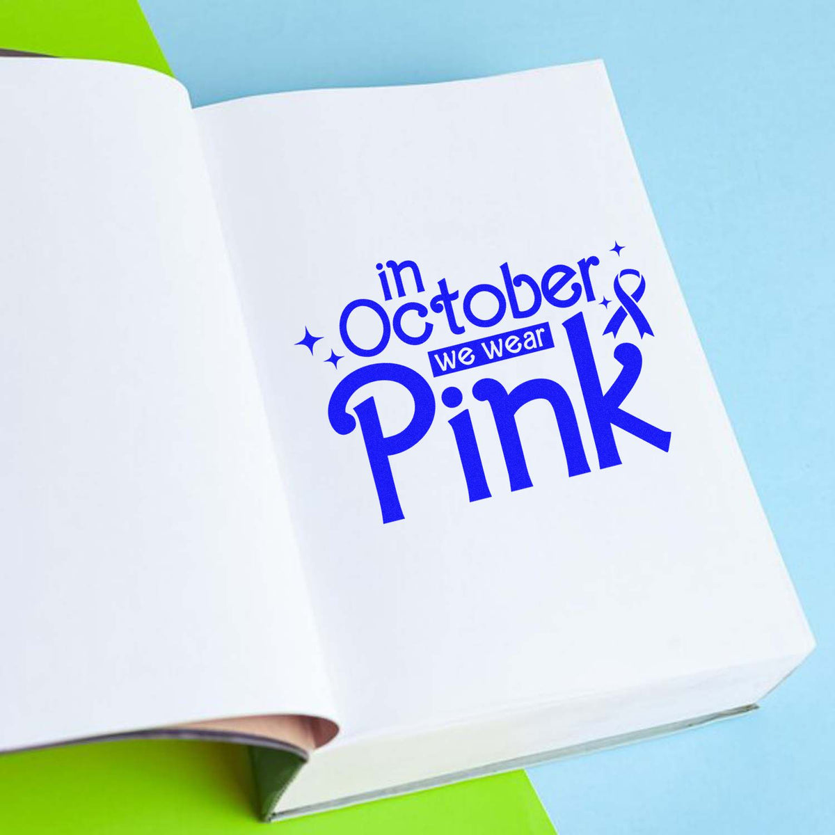 Blue stamp/seal design on white paper reads in October we wear Pink, with ribbon, stars and light blue background.