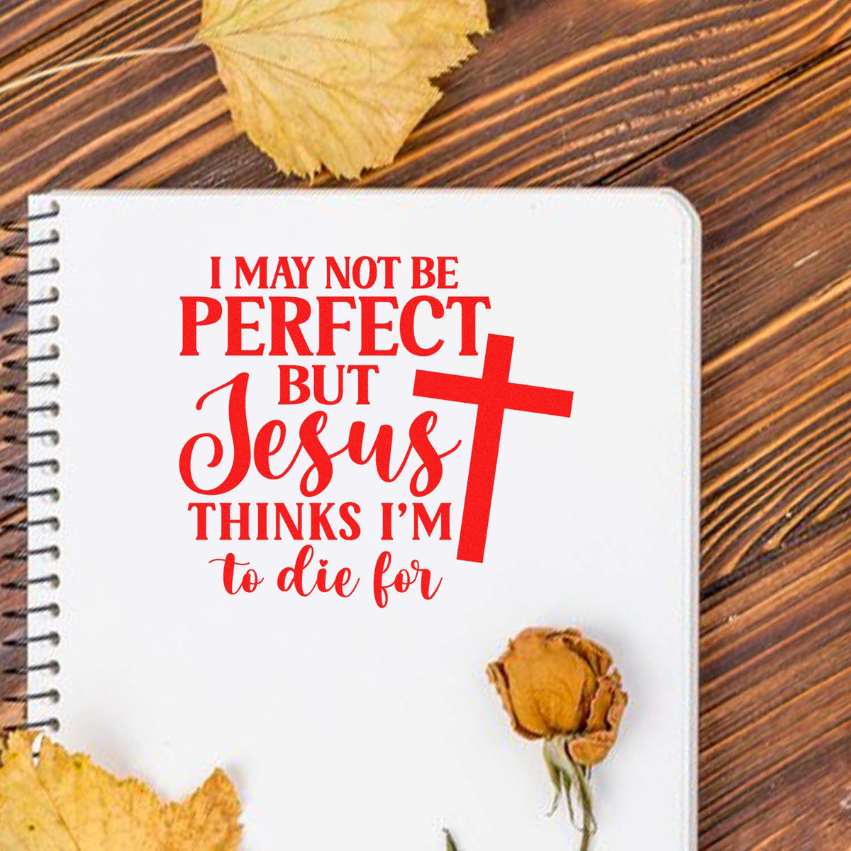 Red Christian stamp and seal design on white notebook, with cross, wood background, and dried leaves.