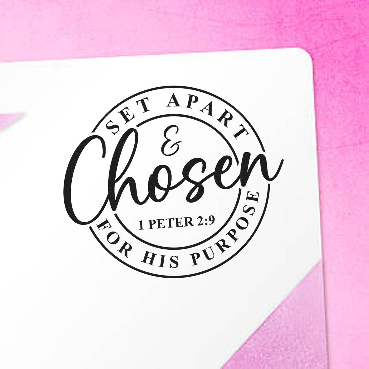 Black circular custom stamp seal reading Set Apart & Chosen for His Purpose on white paper with pink background.