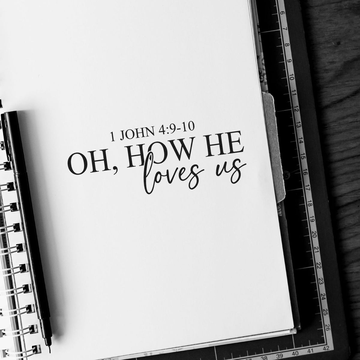Oh How He Loves Us Premium Wooden Stamp - Vintage Pro imprint stamped in black ink. Serif and script lettering reads "Oh, how he loves us," with 1 John 4:9-10 above.