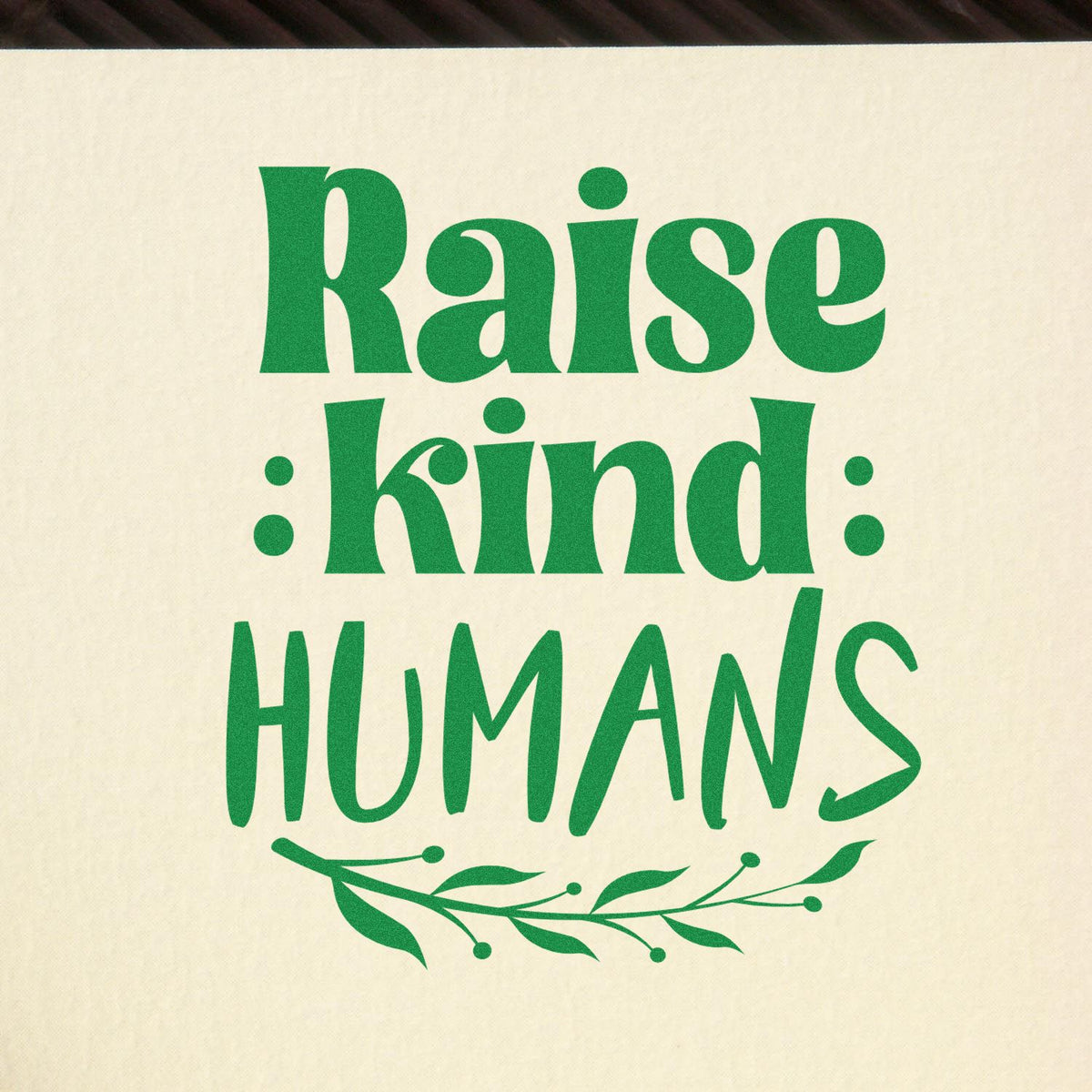 Raise Kind Humans rubber stamp shown in green ink, stamped for projects such as baby shower gifts.