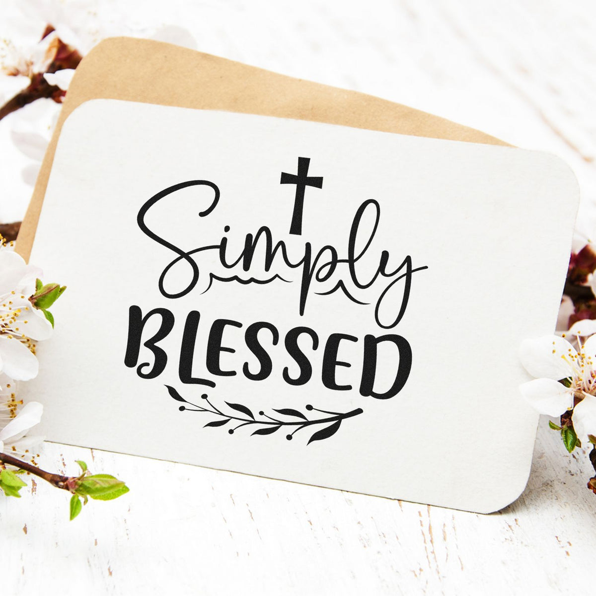 White stamp seal card with black Simply Blessed lettering, cross, and floral accents on a tan backing.