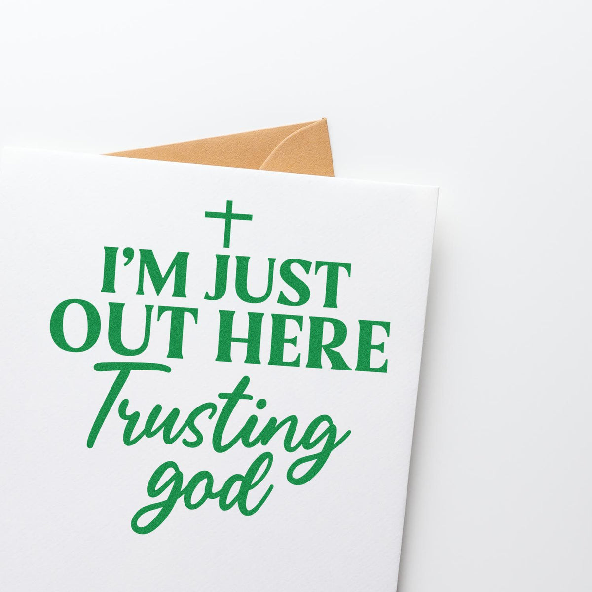 White stamp-and-seal greeting card with green Im just out here trusting God text and a tan envelope.