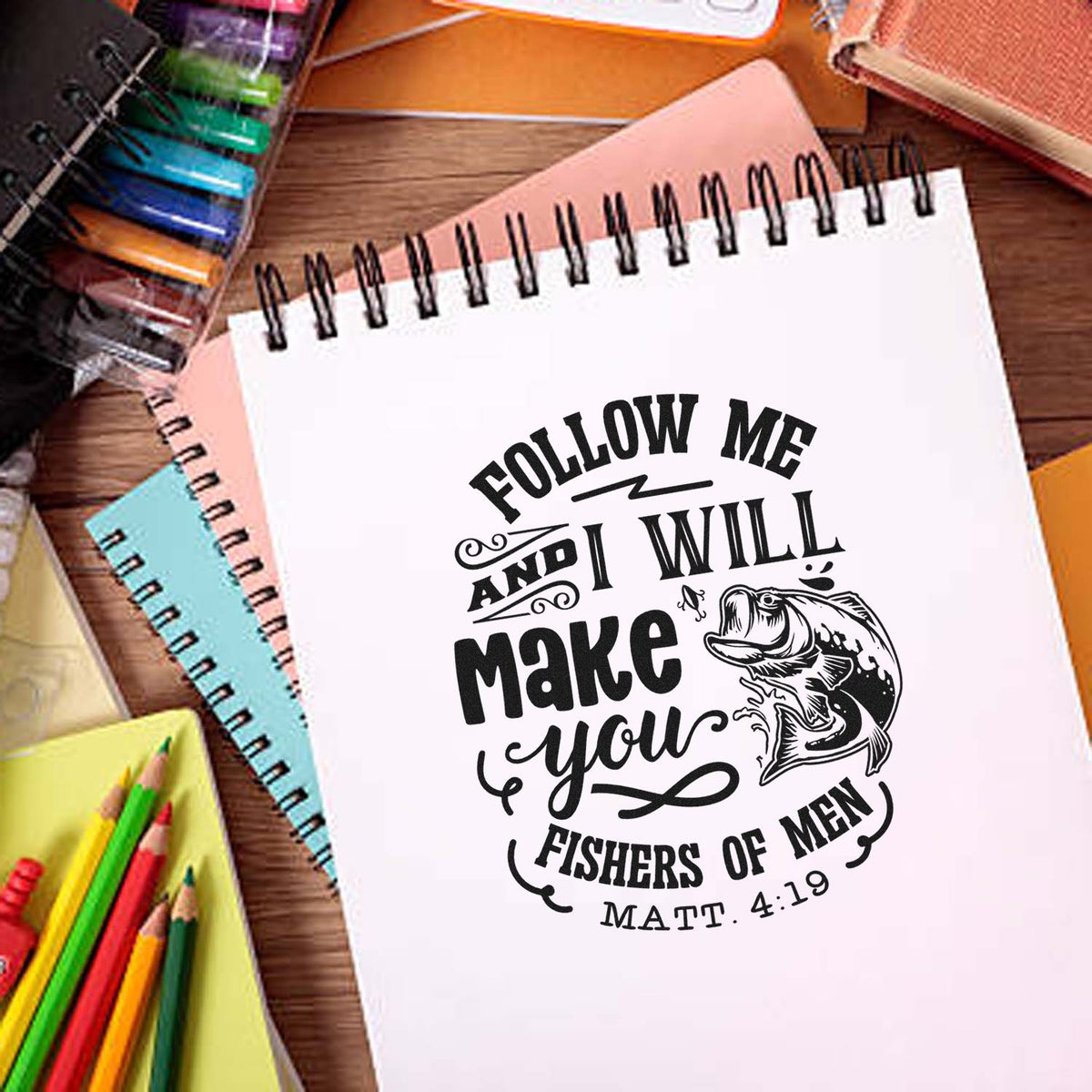 Custom stamp-style seal with fishing quote and black fish on a white spiral notebook, surrounded by colorful notebooks and pencils.