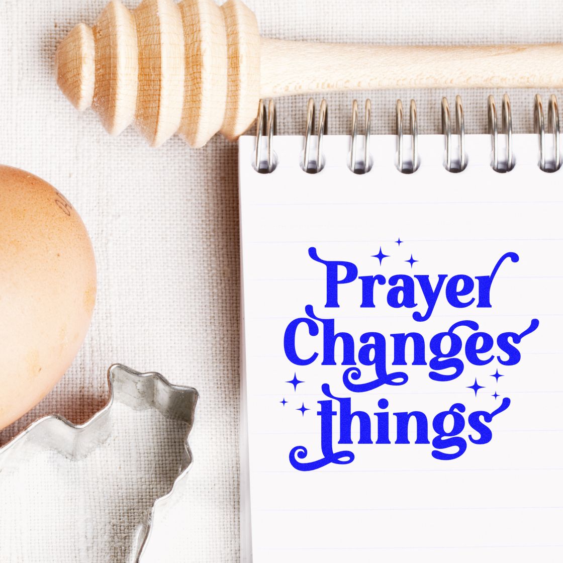 Blue Prayer Changes things stamp on a white spiral notebook beside a wooden seal stamp, egg, and metal cookie cutter.