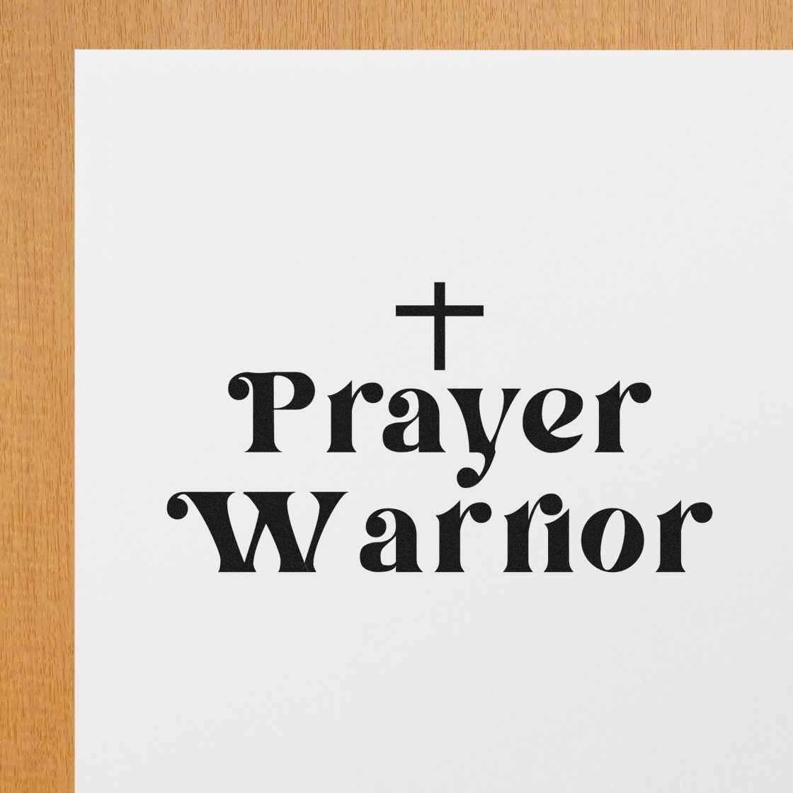 Black Prayer Warrior stamp and seal design with a cross on white paper, set on a light wood background.