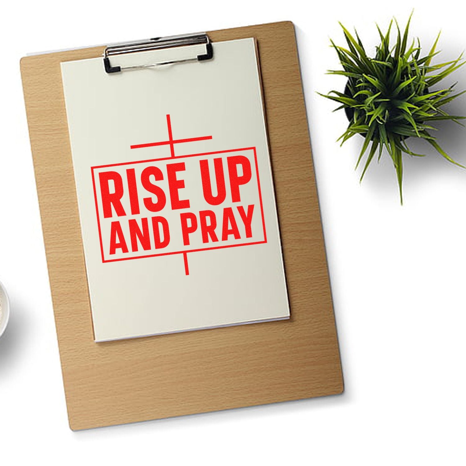 Red rubber stamp reading RISE UP AND PRAY on clipboard, with a green plant beside it.
