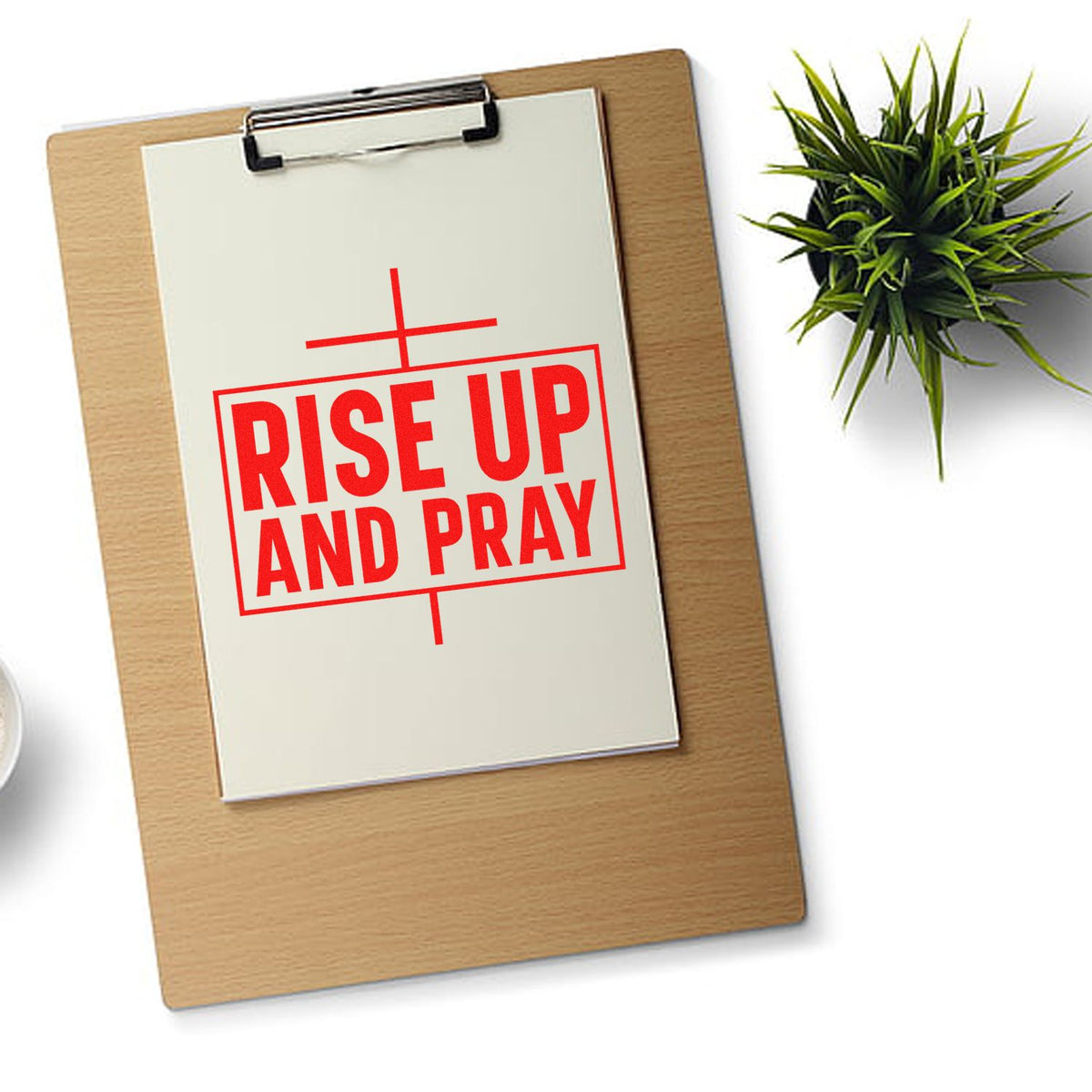 Red stamp seal reading RISE UP AND PRAY on a white clipboard, with a green plant beside it.