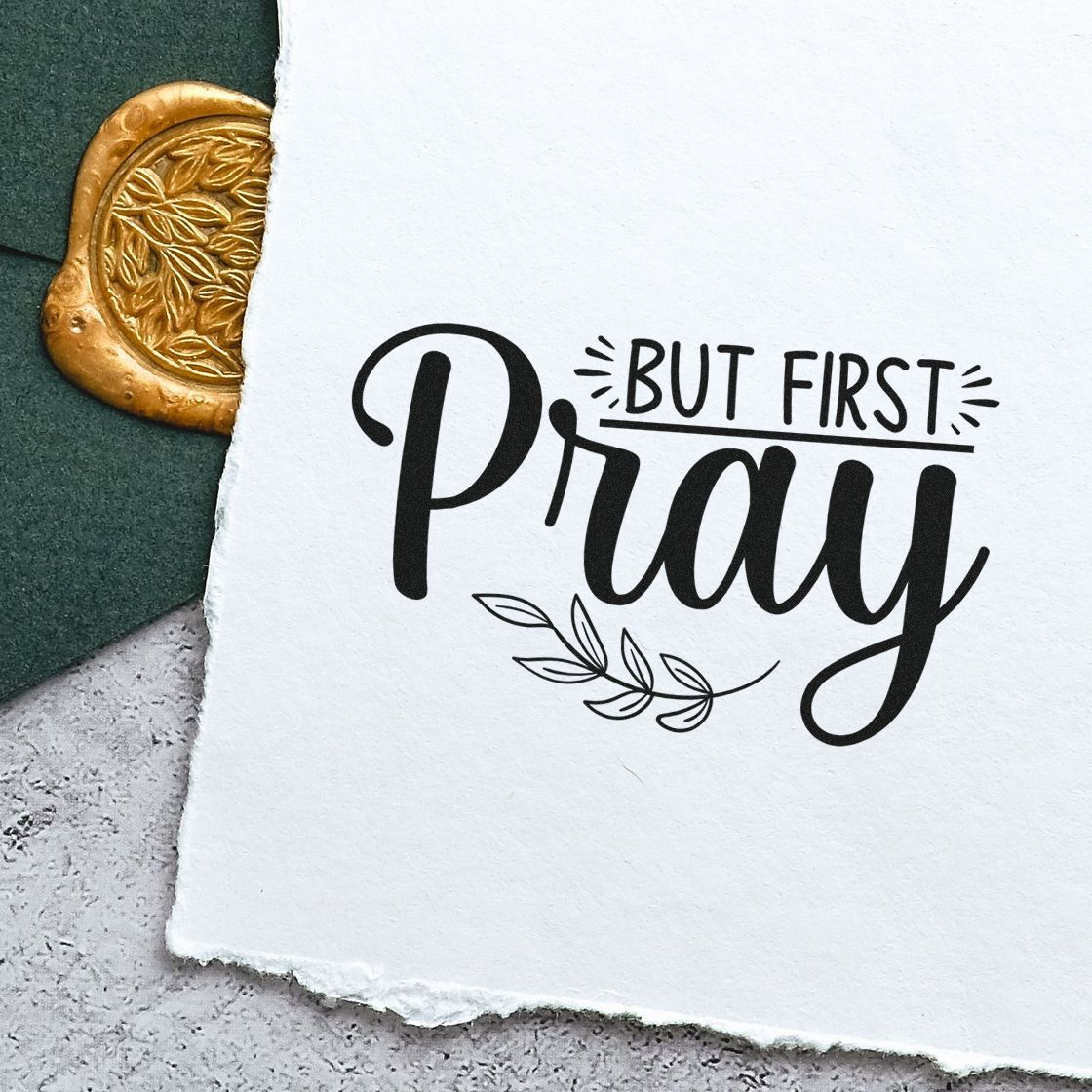 Black But First, Pray stamp on white paper, with a gold embossed wax seal and dark green backdrop.