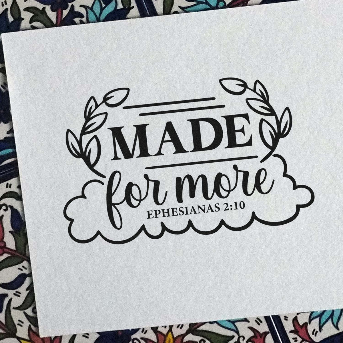 Made For More Leaf Framed Lettering Slim Pre-Inked Stamp imprint stamped in black ink. Leafy sprigs and a scalloped lower border frame "Made for more," with Ephesians 2:10.