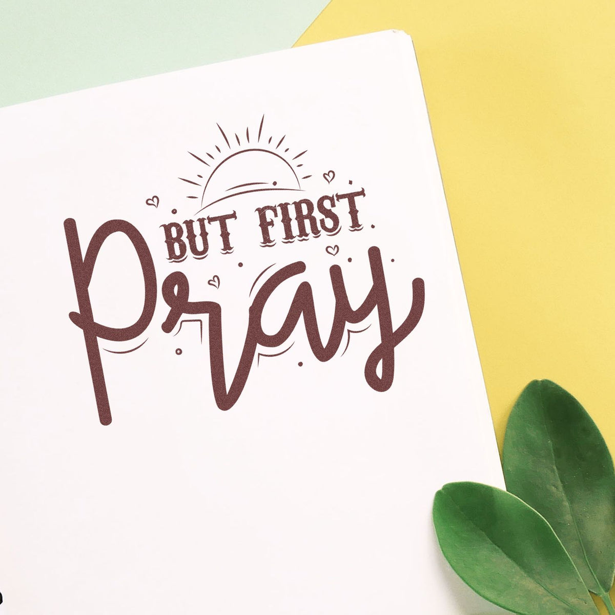 Brown But First, Pray stamp design on a white card with sun doodle, hearts, and green leaves on yellow and mint background.