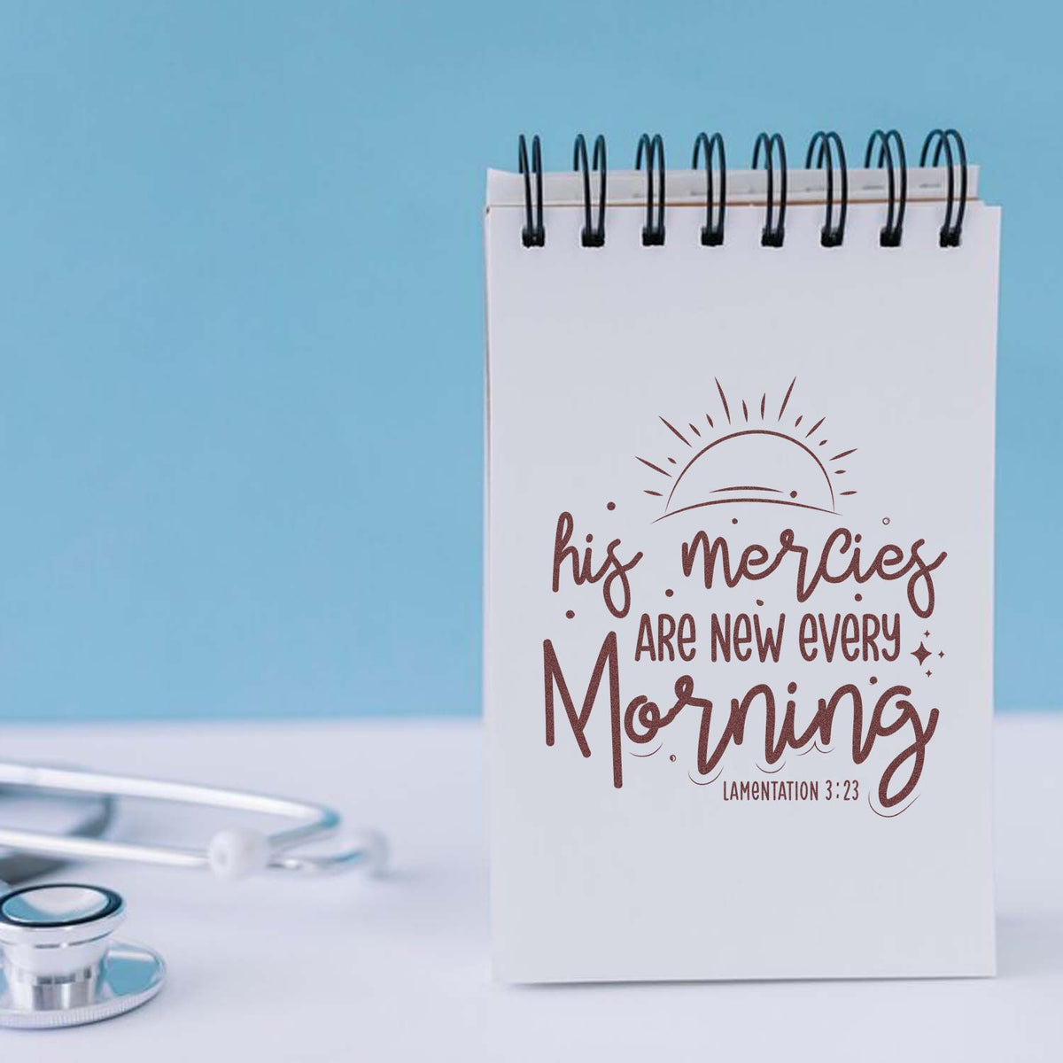 Spiral notepad with brown faith-themed stamp design reading His mercies are new every morning on a light blue background.
