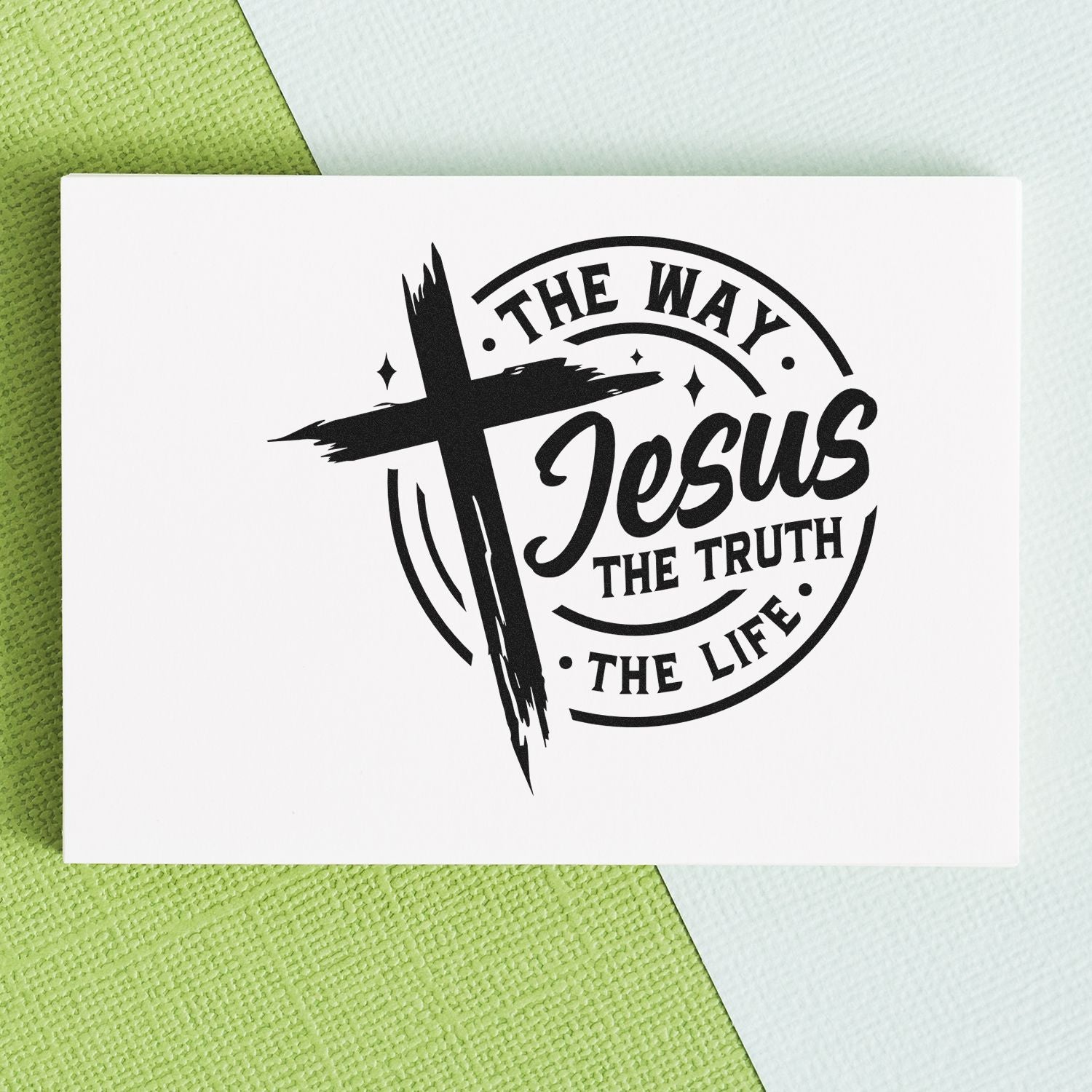 Black religious stamp seal design with cross and The Way, Jesus, The Truth, The Life in black on a white card over green background.