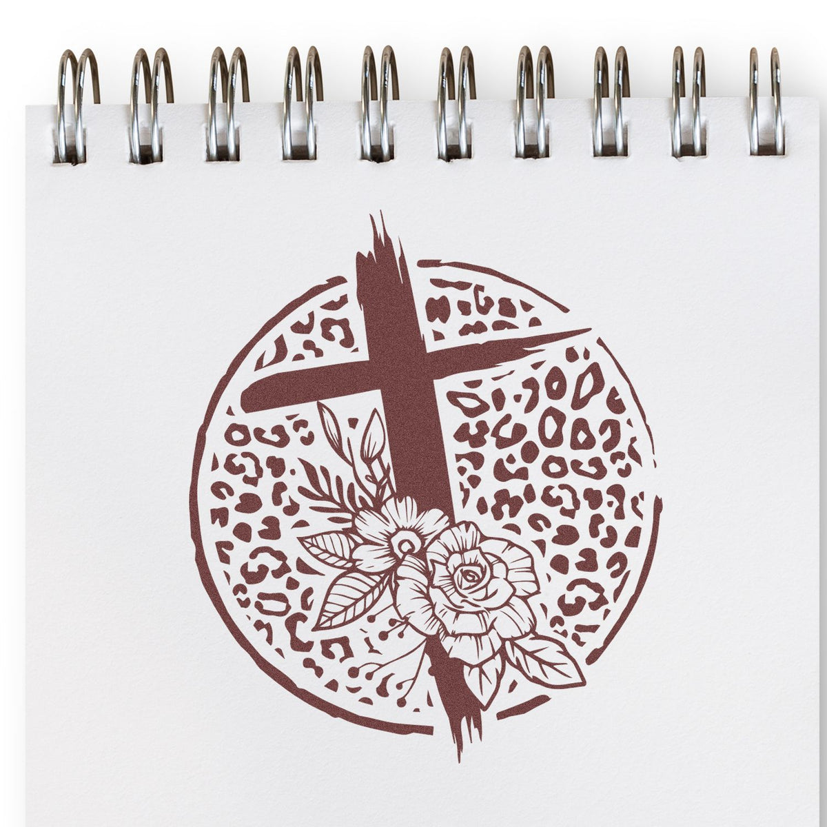 Brown circular cross and floral seal stamp design on white spiral notebook, with leopard print and flower details.