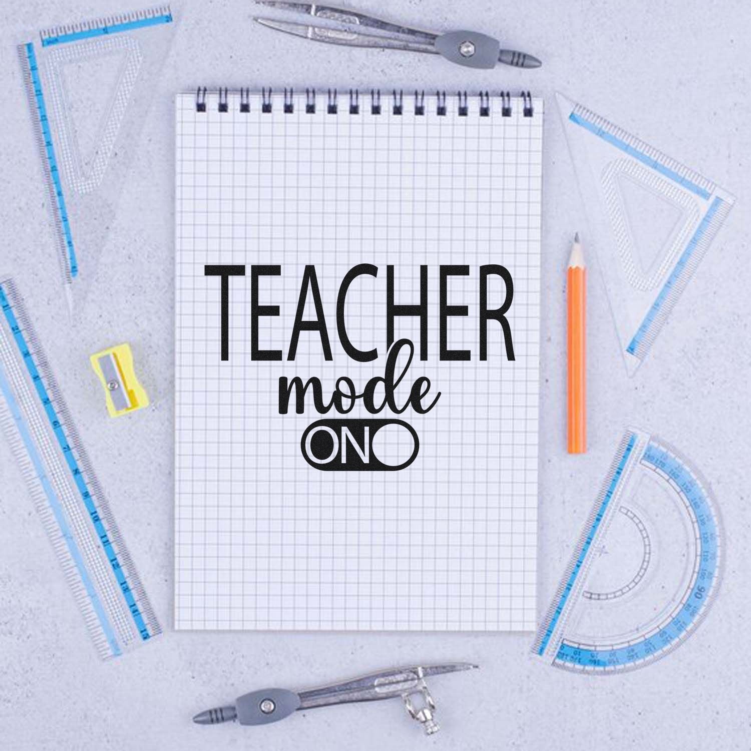 Black Teacher Mode On stamp on graph paper, framed by blue drafting tools, an orange pencil, and silver compasses.
