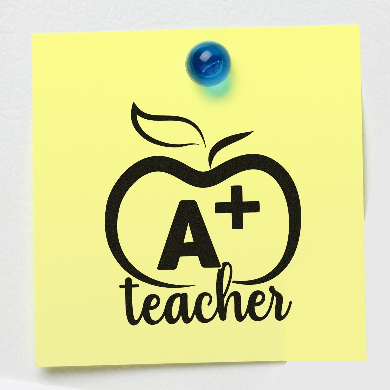 Yellow sticky note with black A+ teacher apple stamp/seal design and blue pushpin