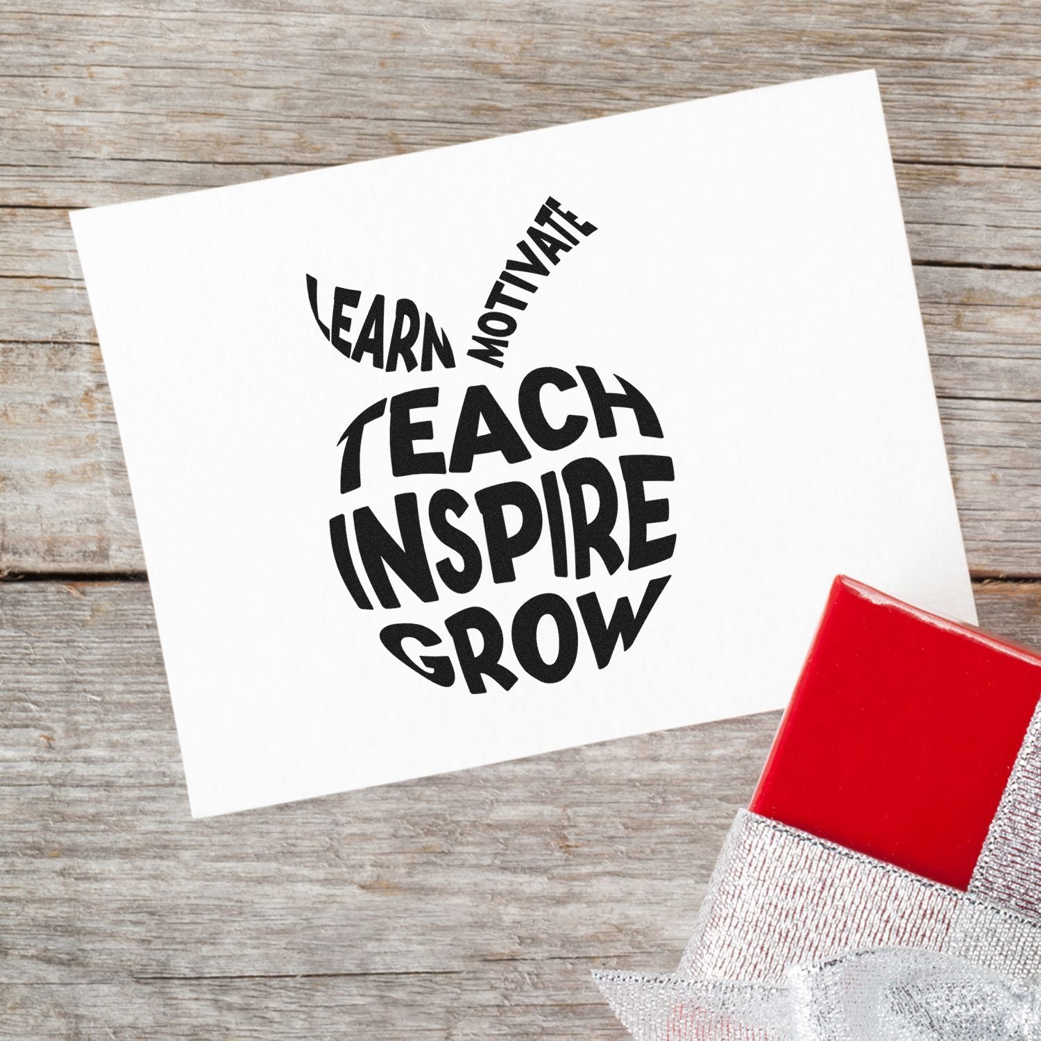 Black motivational stamp reading Teach Inspire Grow on white paper, with red seal stamp block on rustic wood.