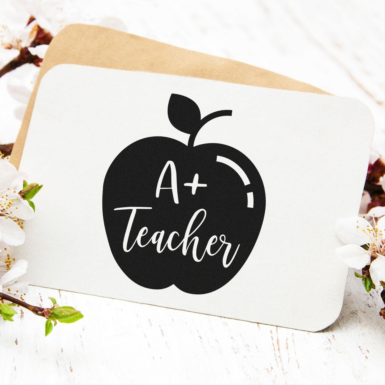 Black apple-shaped A+ Teacher stamp seal on white card with tan backing and white blossoms