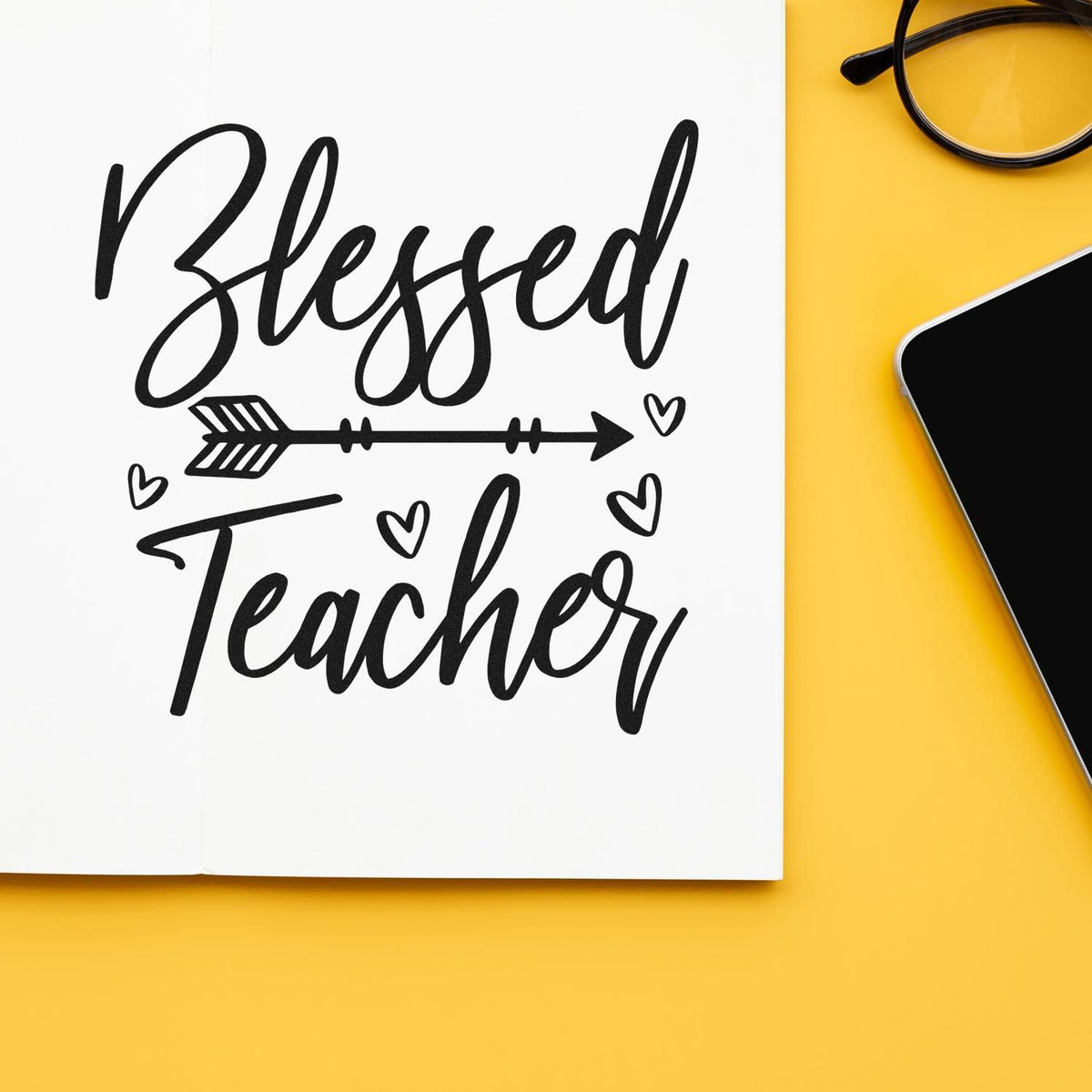 Black Blessed Teacher stamp seal in script with arrow and hearts on white, beside glasses and phone on yellow background
