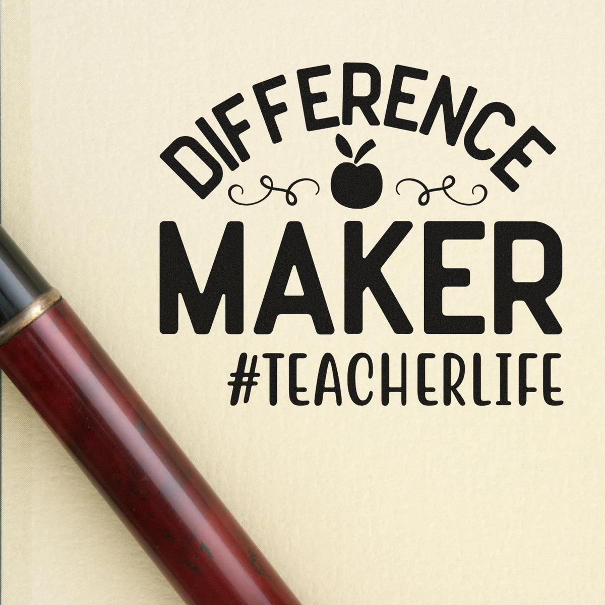 Black teacher stamp reading DIFFERENCE MAKER #TEACHERLIFE with apple icon and red wooden handle on cream background