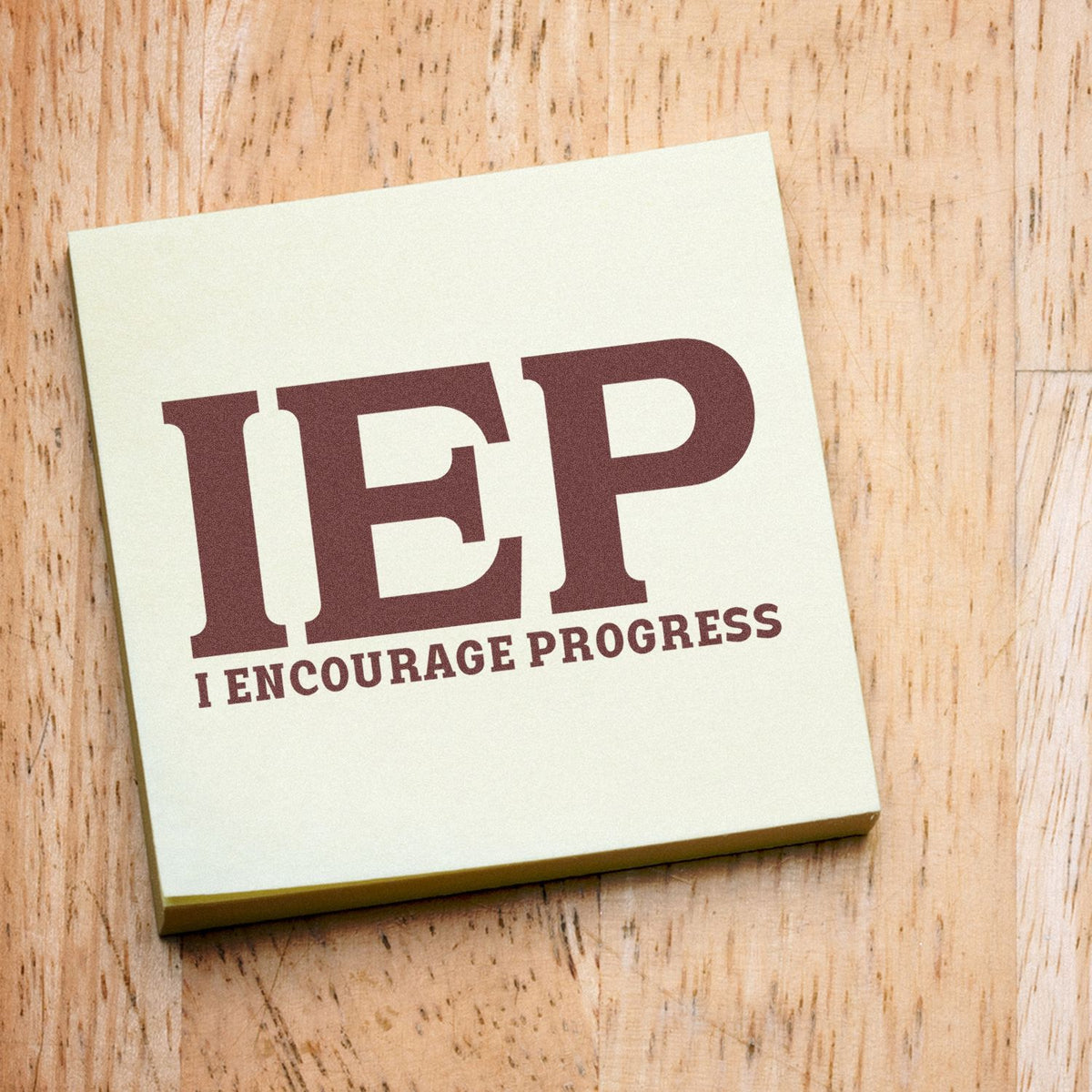 Maroon IEP rubber stamp seal on cream pad, reading I Encourage Progress, on a light wood surface.