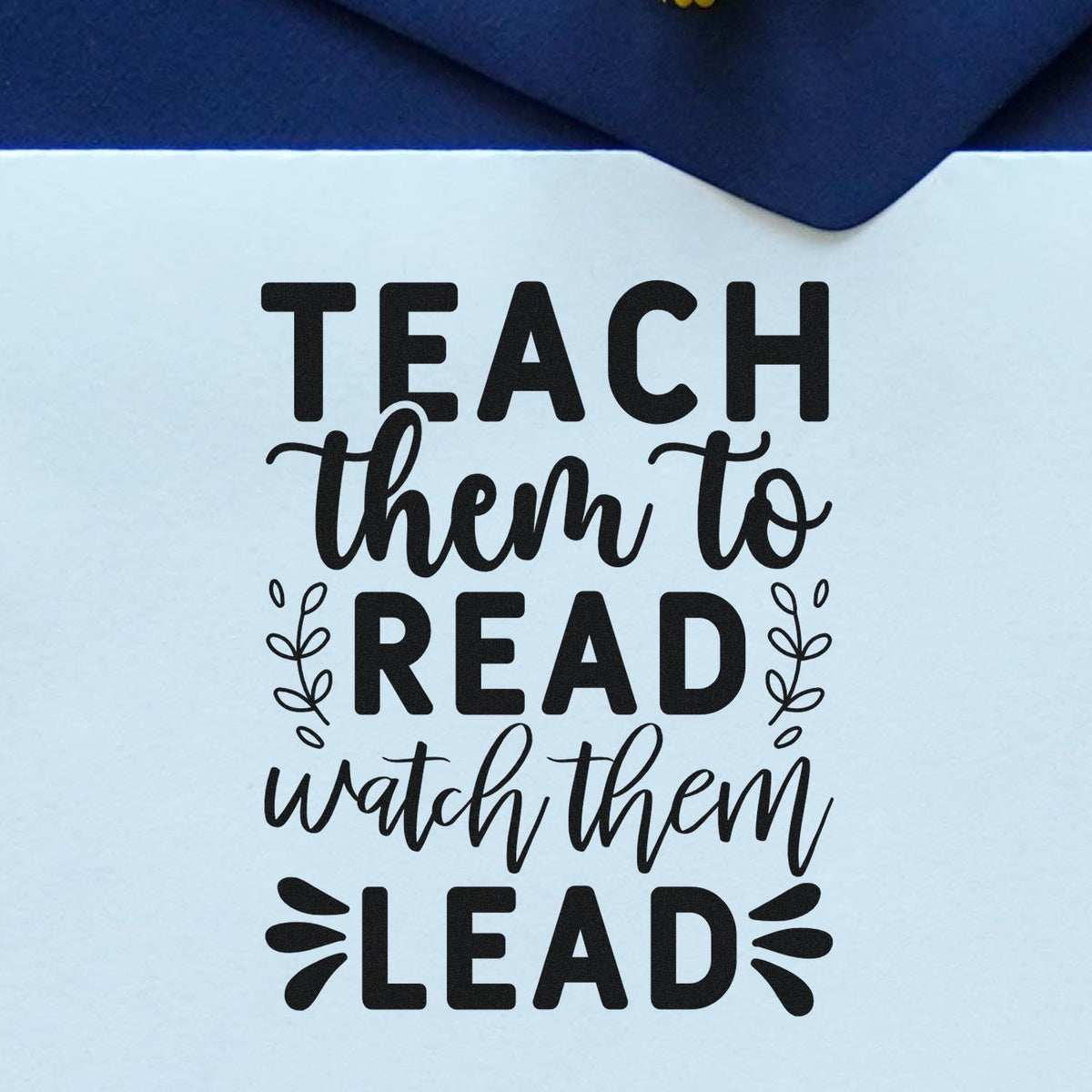 Black teacher stamp design on light blue paper, reading Teach them to read, watch them lead, with navy accent.