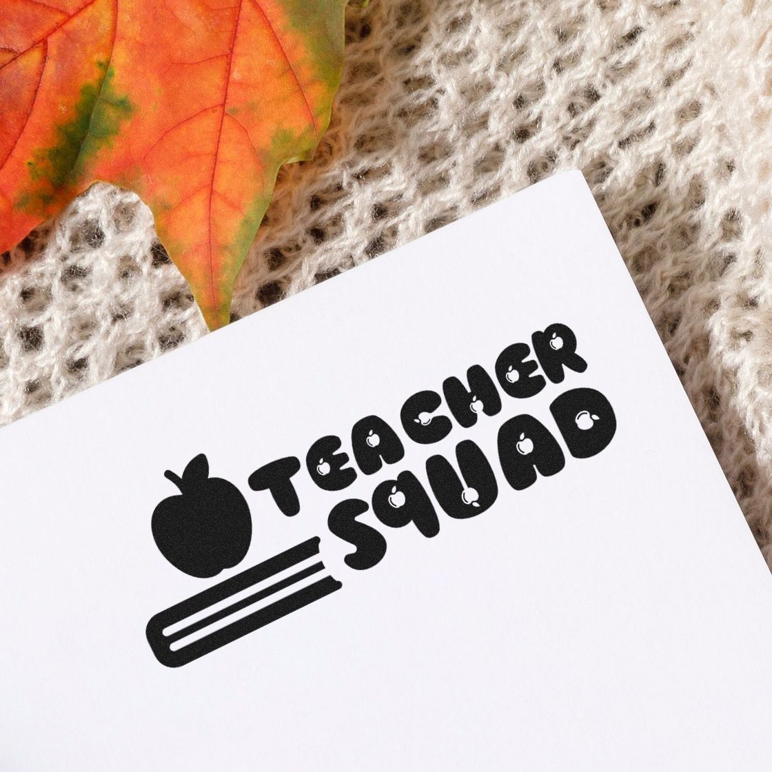 Black Teacher Squad stamp/seal logo with apple and comb icon on a white card, on a cozy knit background with an autumn leaf.