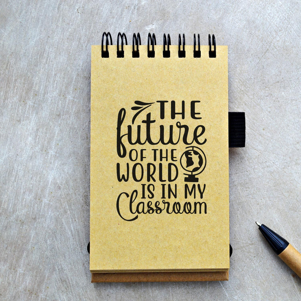 Yellow spiral notebook with black classroom stamp, globe seal and quote: The future of the world is in my classroom.