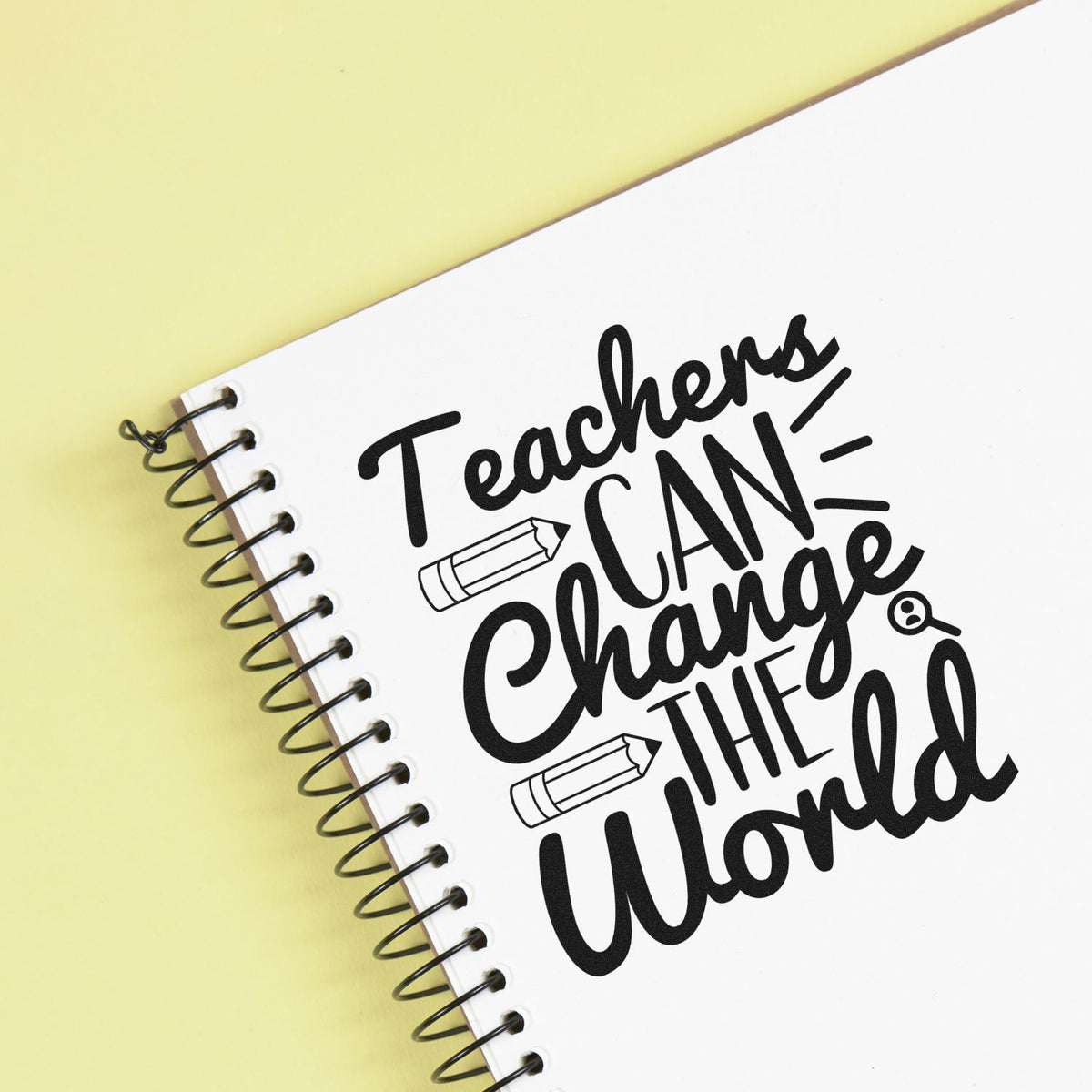 Black teacher stamp and seal design on white spiral notebook with pencil icons, set against a pale yellow background.