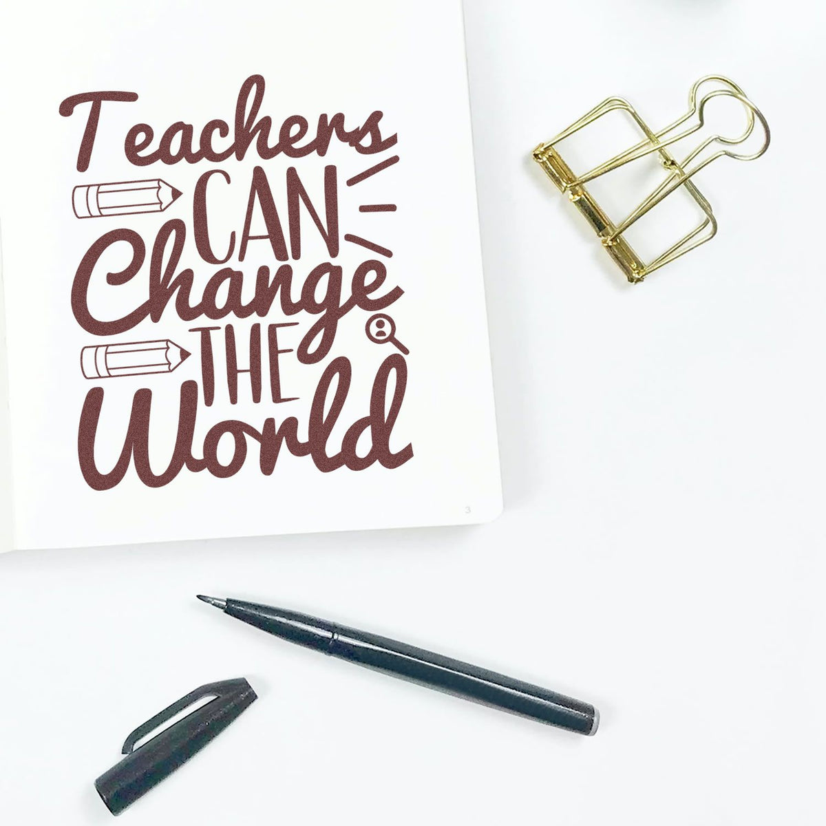 Brown "Teachers Can Change the World" stamp/seal design on white card, with gold binder clip and black pen.