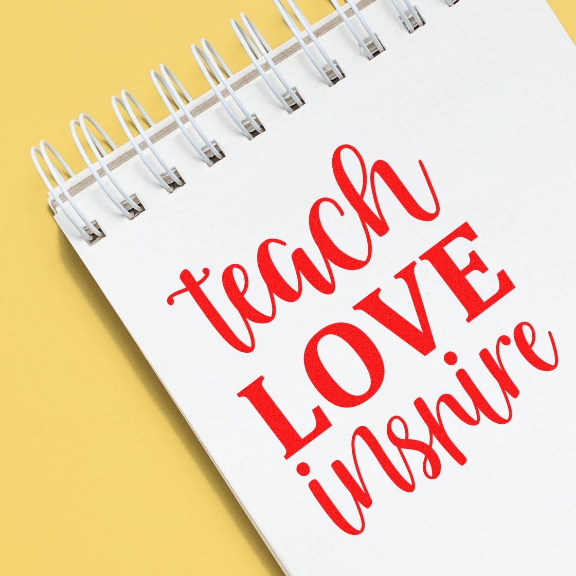 Red "teach LOVE inspire" stamp on a white spiral notebook page, with a yellow background for stamp and seal products.