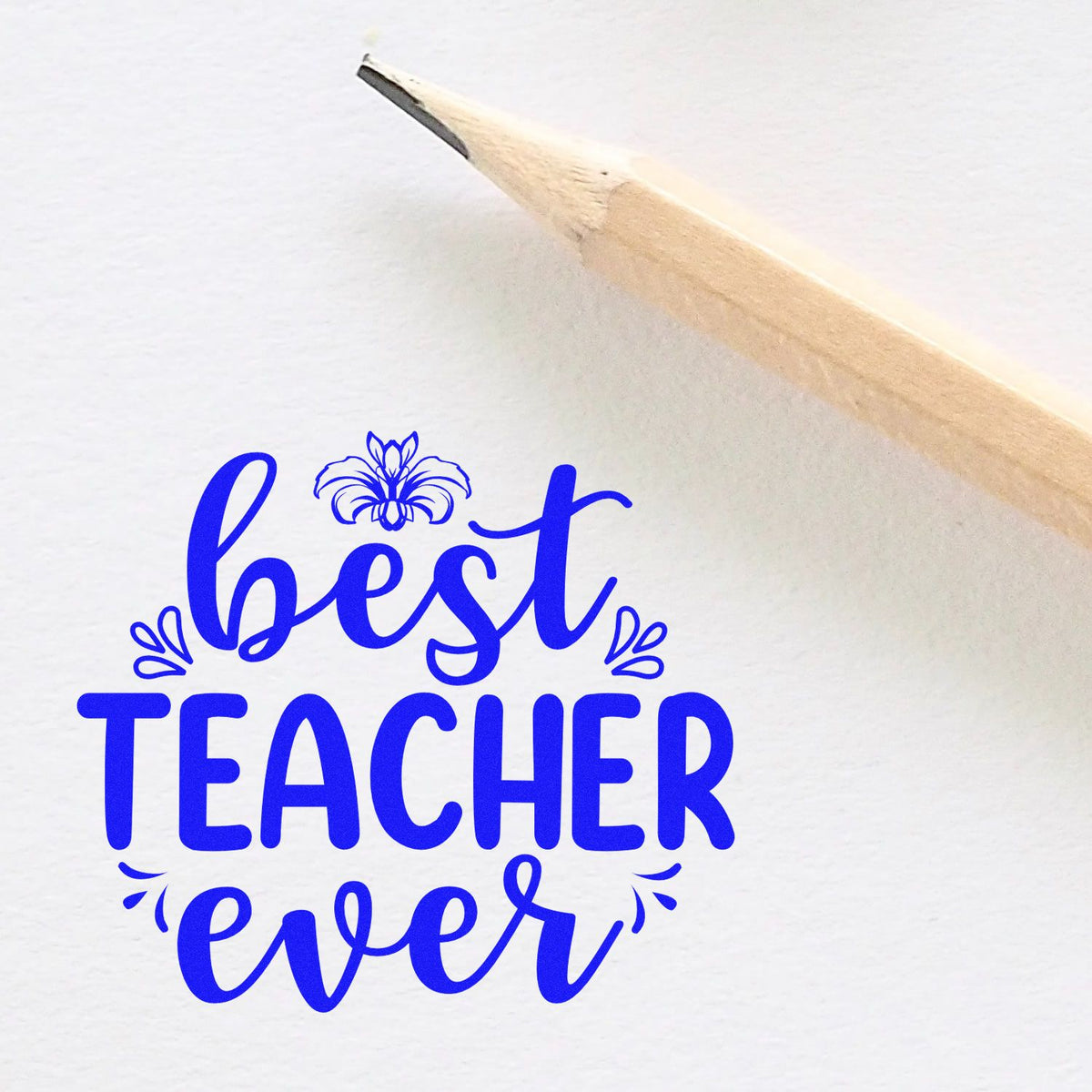 Blue best TEACHER ever stamp impression with decorative flourishes beside a pencil on white paper.