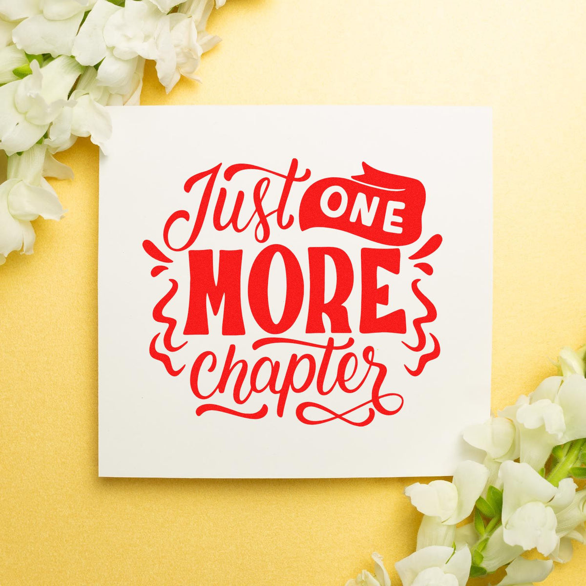 Red Just One More Chapter stamp and seal on a white card, with white flowers on a pale yellow background.