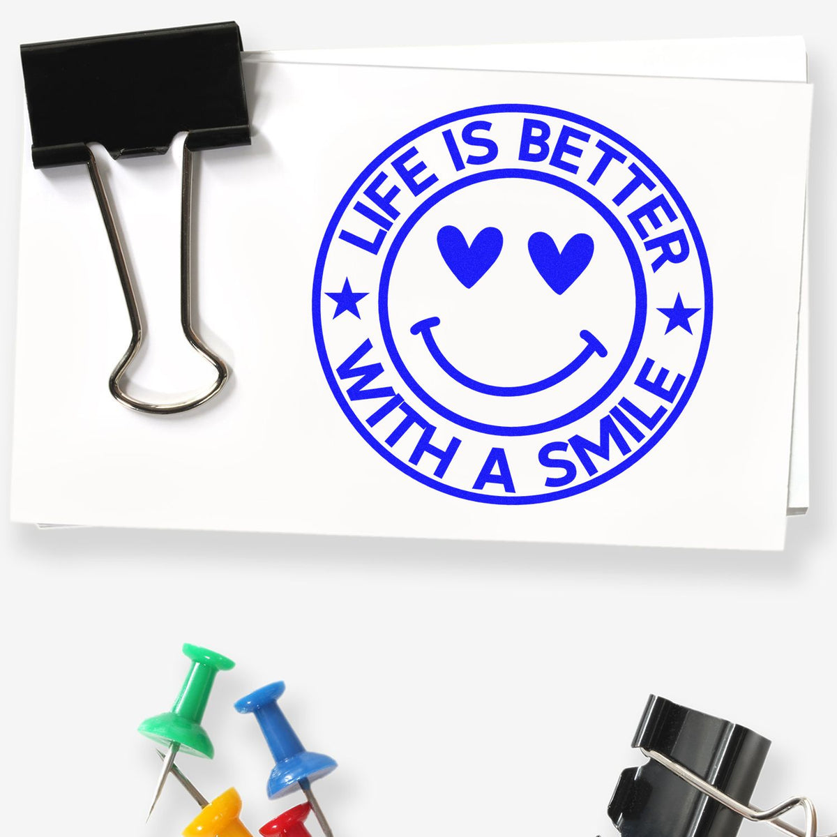 Blue Life Is Better With a Smile stamp seal on white paper, with heart eyes, smiley face, binder clip and pushpins.