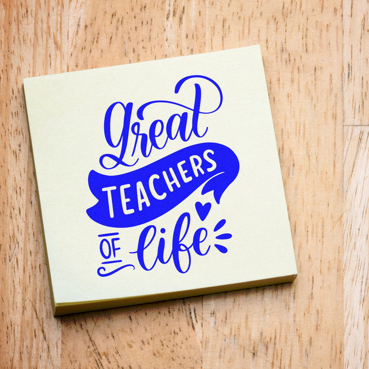 Blue Great Teachers of Life stamp seal on a cream square card, resting on a light wood background.