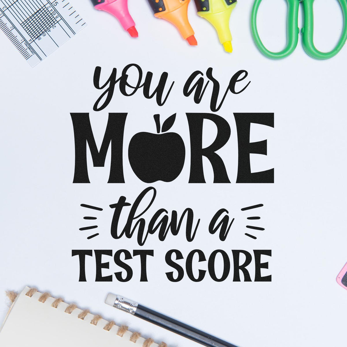 You Are More Than A Test Score Slim Pre-Inked Stamp imprint stamped in black ink. “You Are More Than a Test Score” incorporates an apple into “More.”