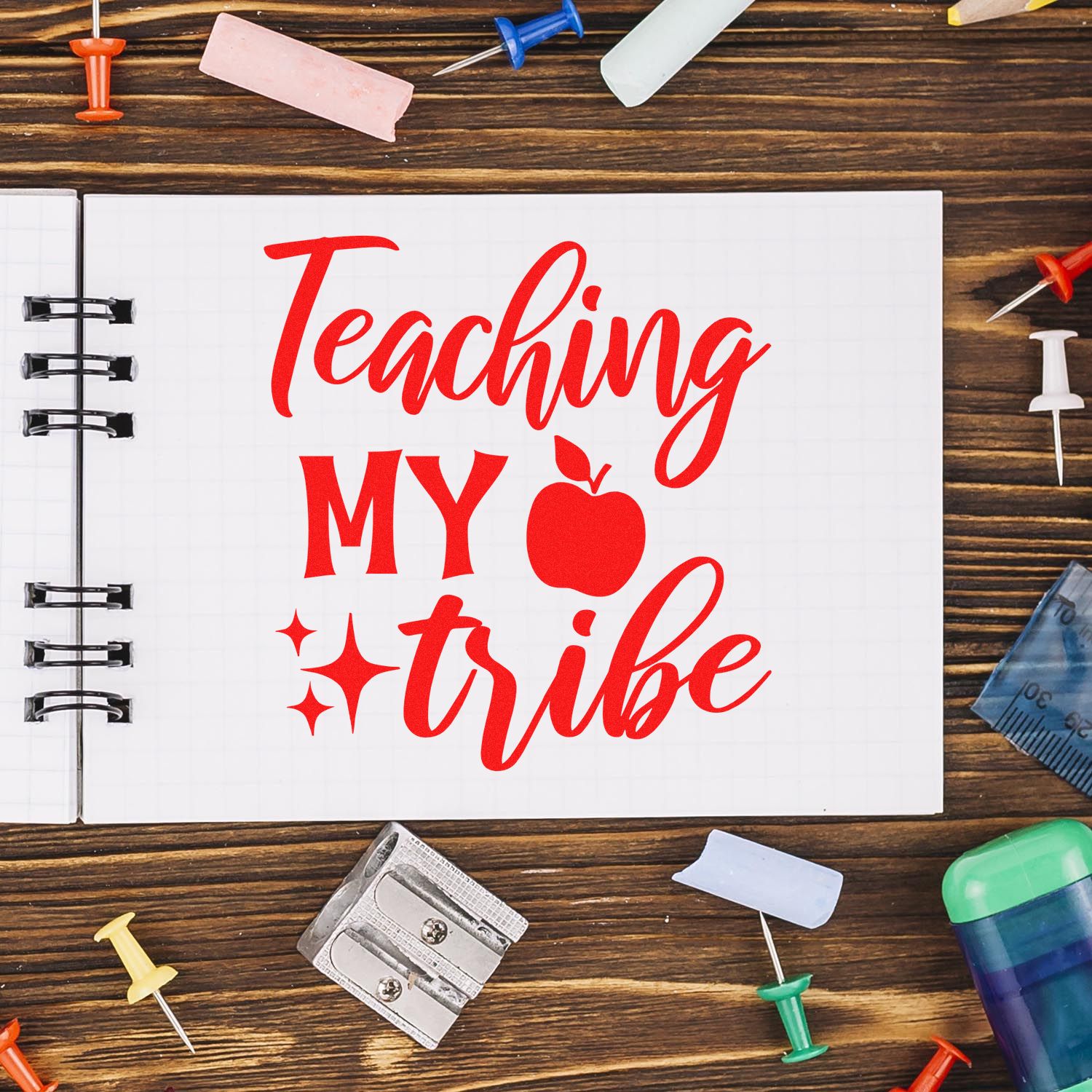 Red Teaching my tribe rubber stamp seal on notebook, surrounded by colorful school supplies on a wood table.