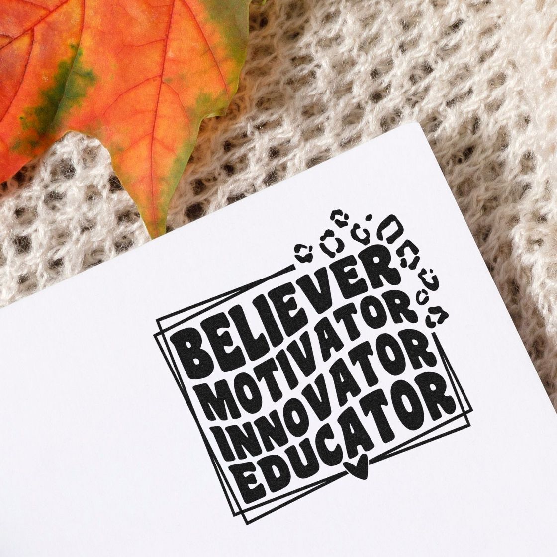 Black educator motivational stamp and seal on white paper, with leopard-print accents, orange leaf, and beige knit background.