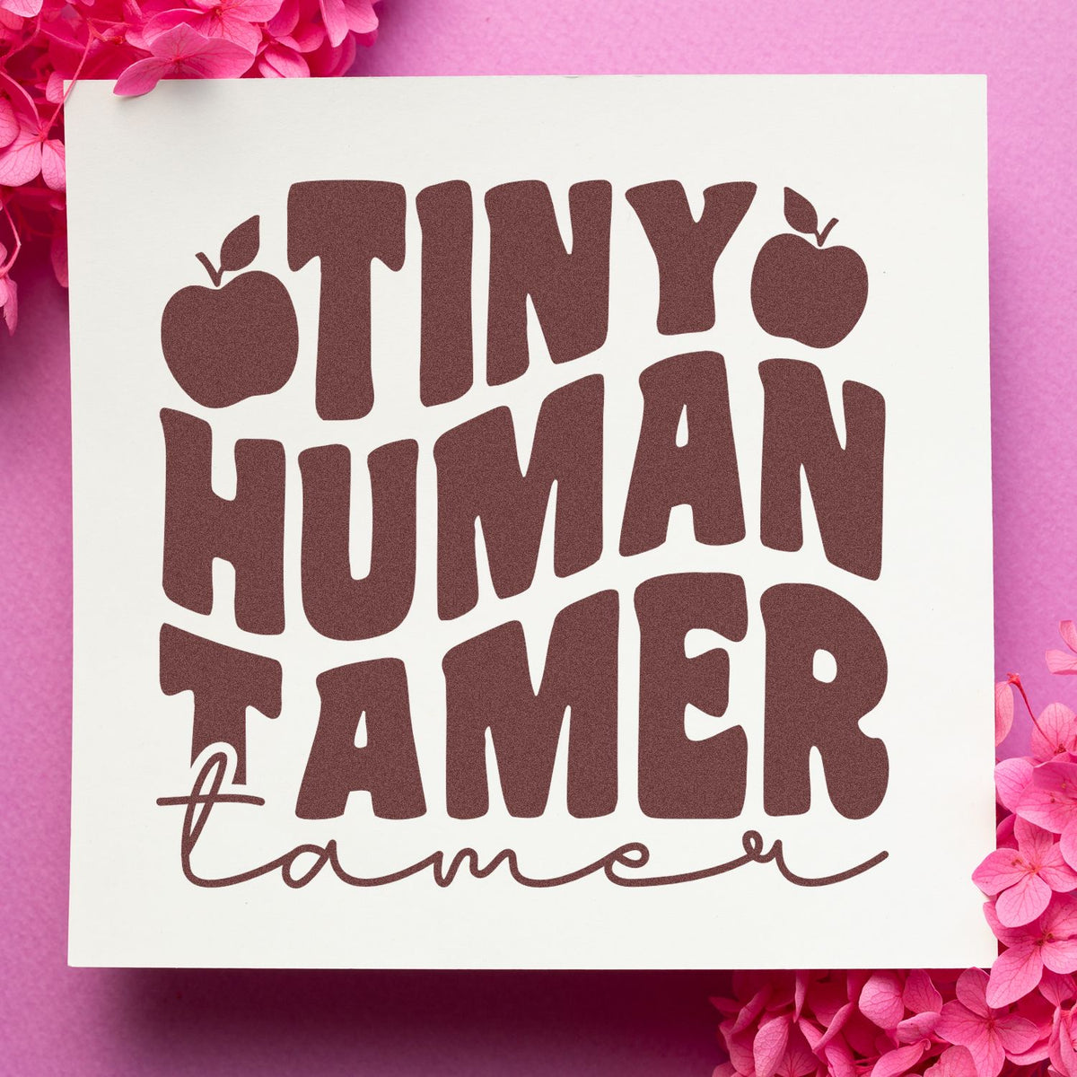 Brown Tiny Human Tamer stamp seal on white, set against a pink background with bright pink flowers.