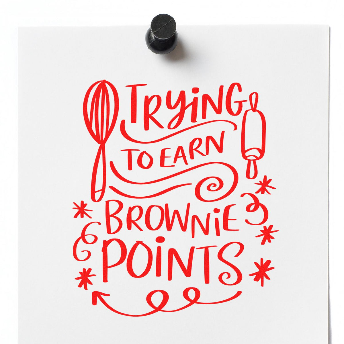 Red rubber stamp design on white paper with whisk and rolling pin, reading Trying to earn brownie points; black stamp handle above.