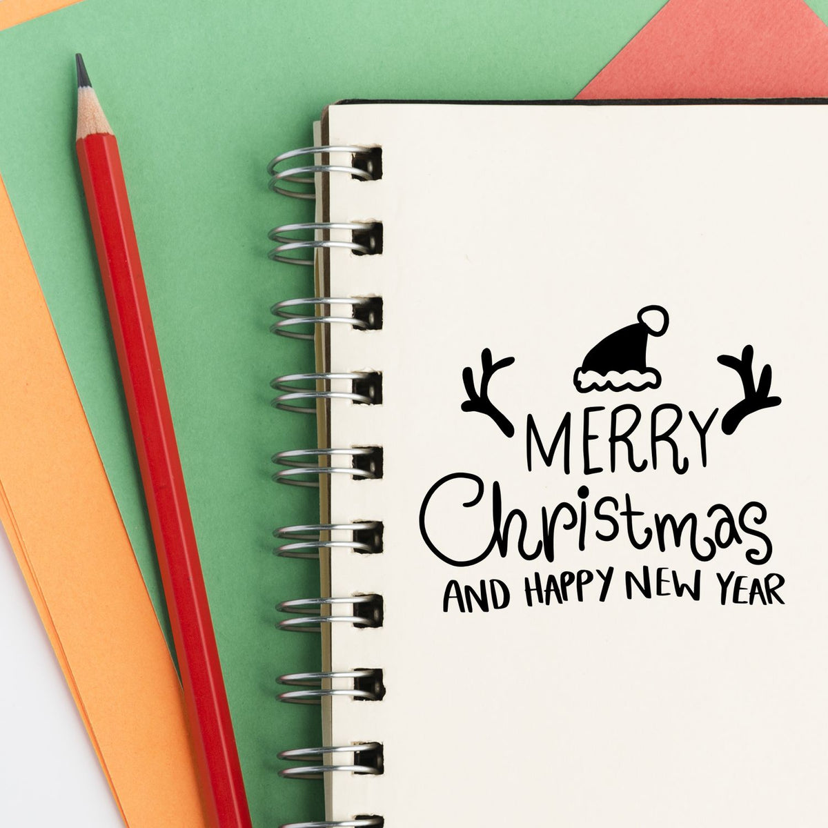 Christmas stamp and seal design on a spiral notebook, with Merry Christmas and Happy New Year text on green, red and orange paper.