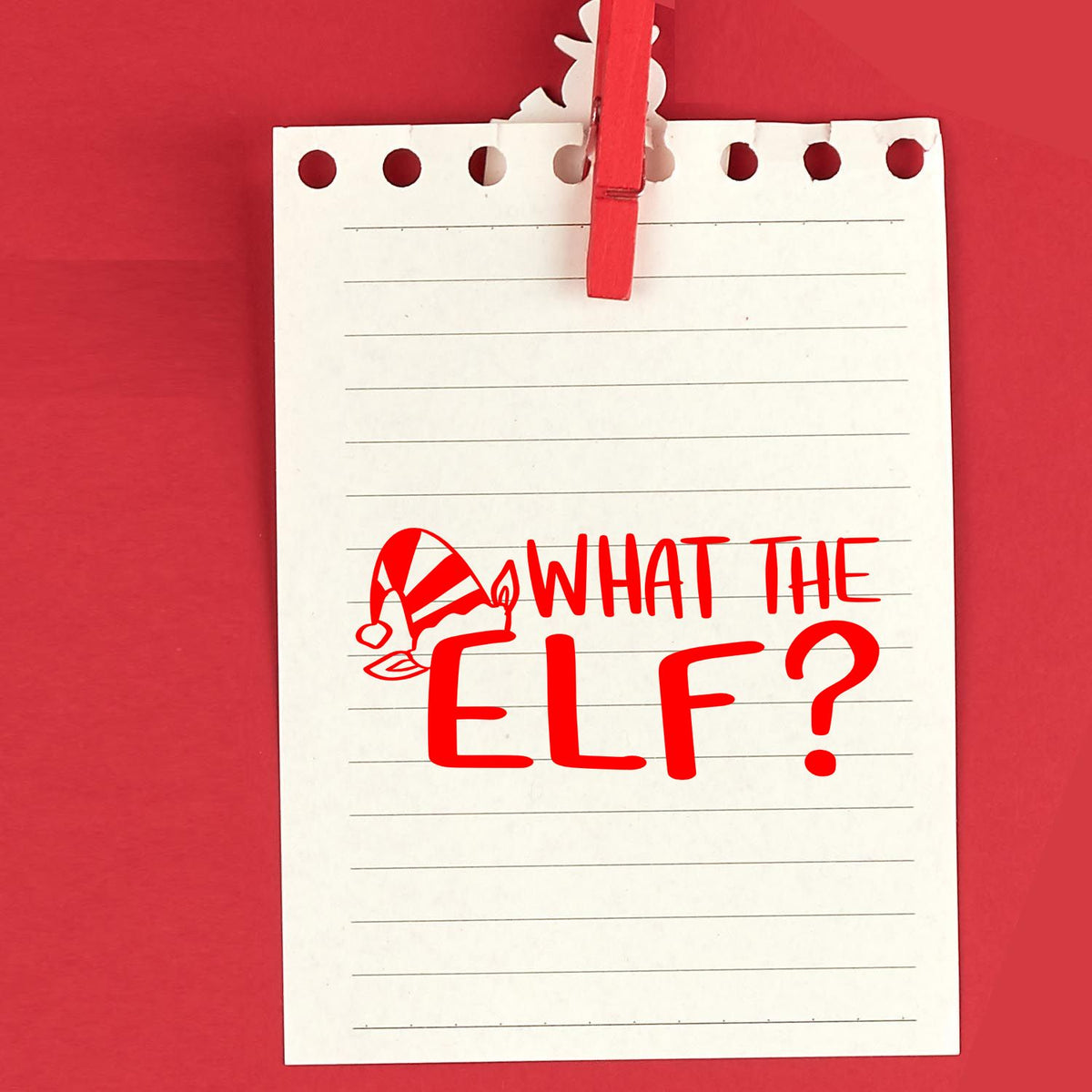 Red holiday stamp and seal reading What the Elf? on a white lined notepad clipped with a red clothespin.